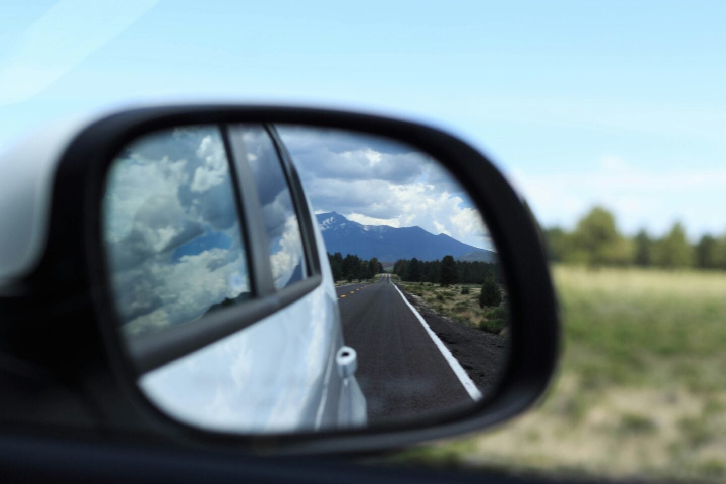 Open road and distant mountains reflected in a car side mirror during a scenic road trip