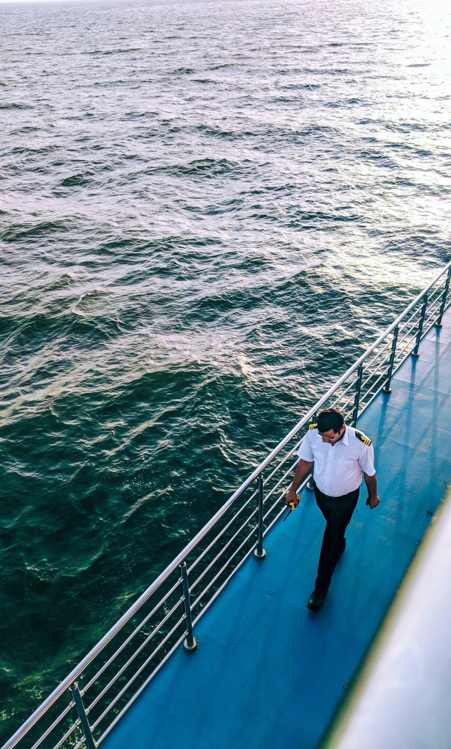 A uniformed crew member walking along the deck of a ship with the ocean in the background.