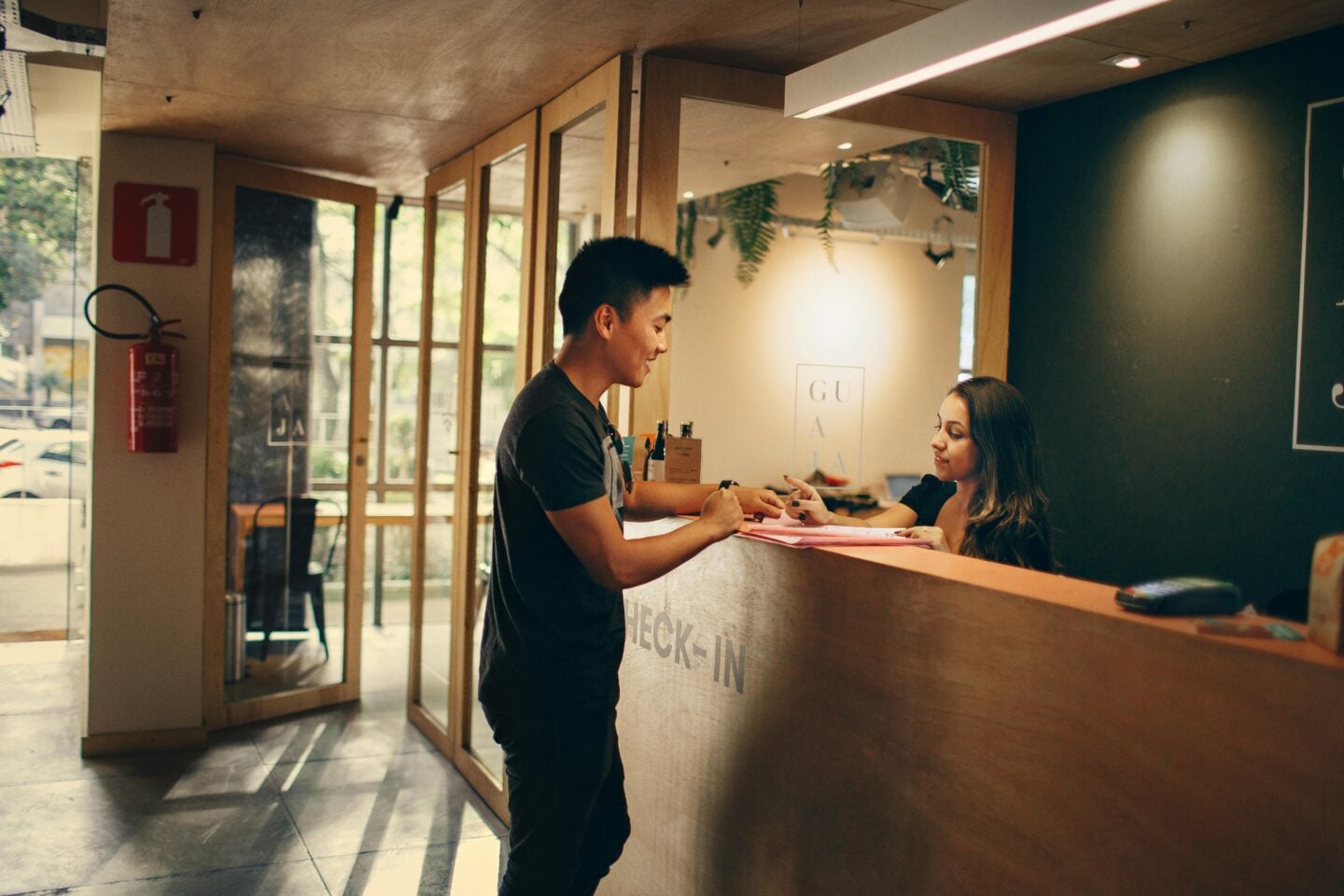 A hotel receptionist assisting a guest at the check-in counter inside a bright, modern lobby.