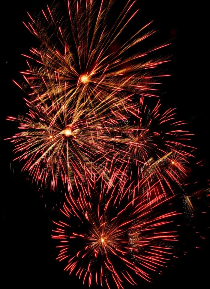 Red and gold fireworks bursting in the night sky, creating bright streaks and starburst patterns against a dark background.