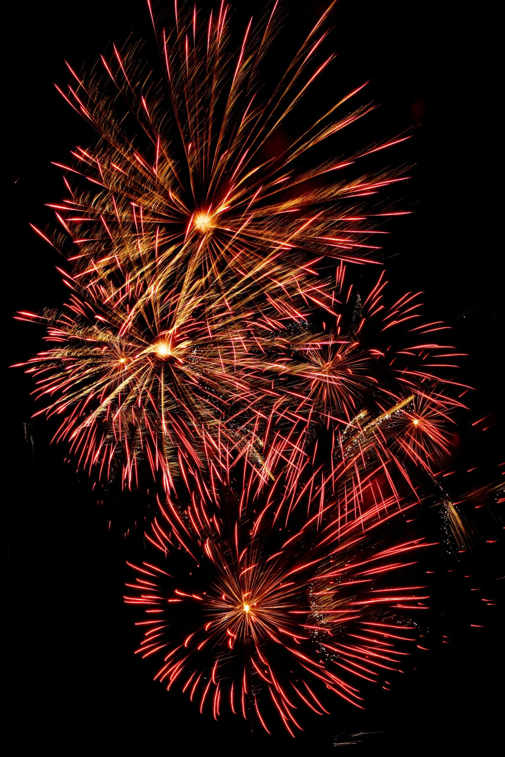 Red and gold fireworks bursting in the night sky, creating bright streaks and starburst patterns against a dark background.