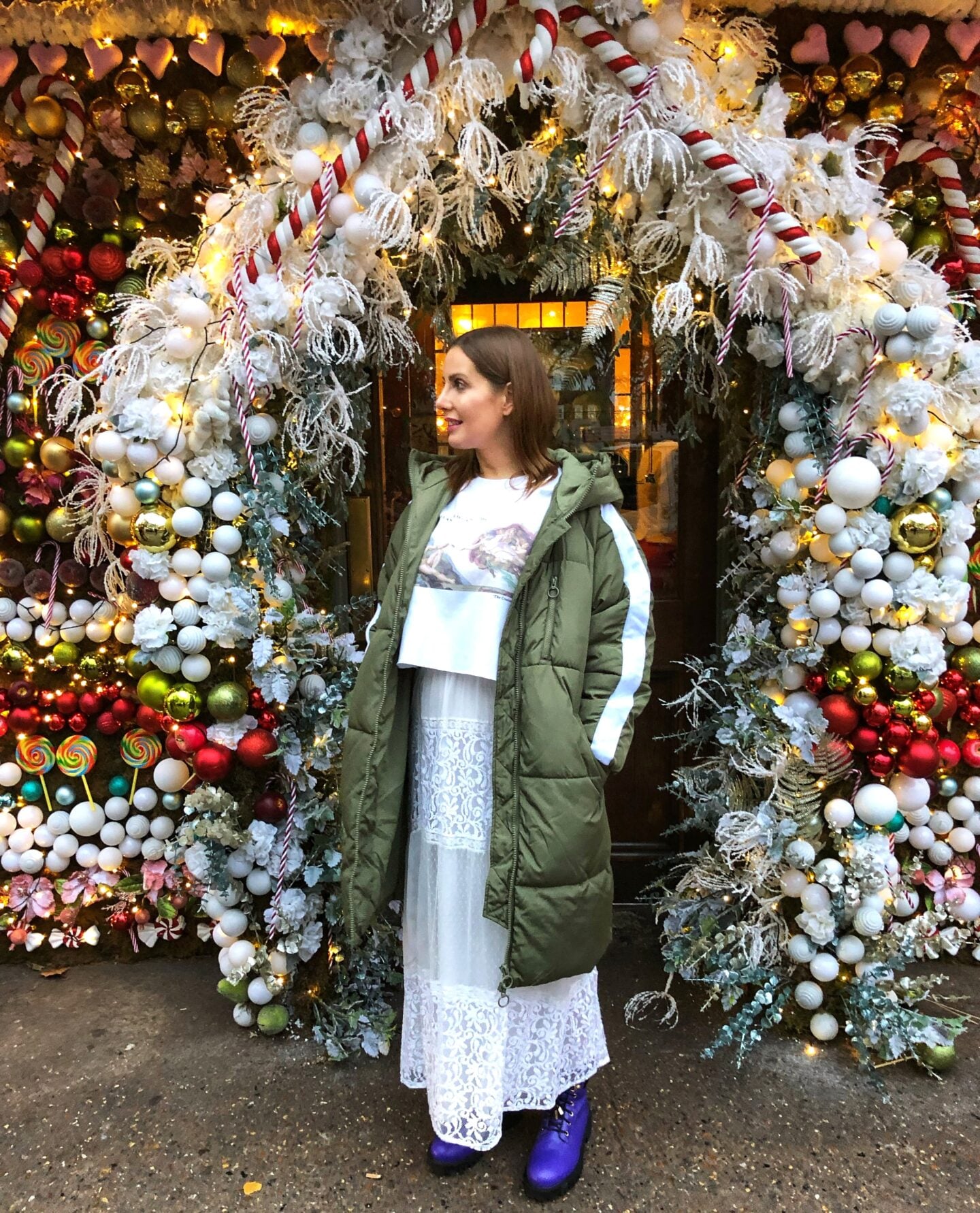 A woman standing under a colourful Christmas archway decorated with candy canes, baubles, and winter foliage in London, capturing the magical holiday atmosphere of the city.