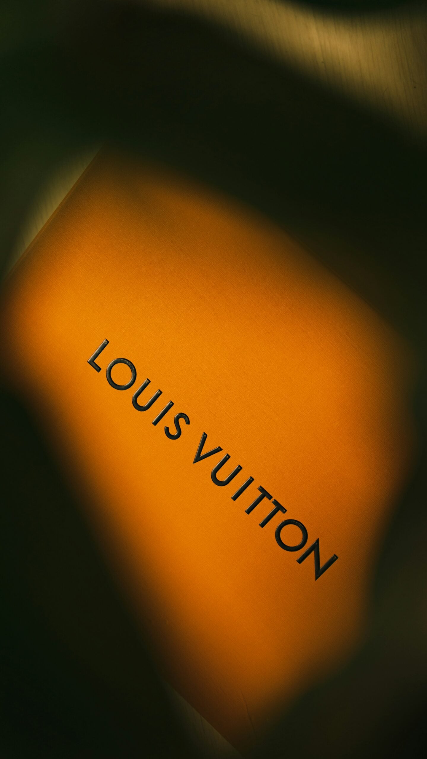 A close-up of an orange Louis Vuitton box partially shaded, highlighting the brand’s iconic black lettering.