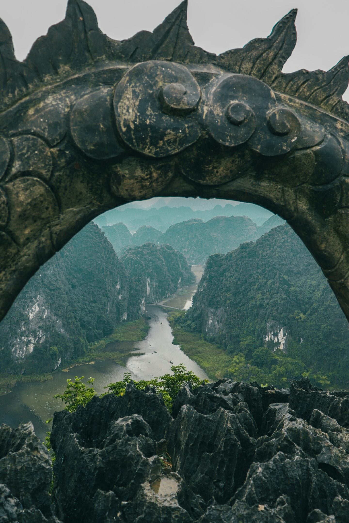 Limestone karst landscape and winding river framed by stone arch viewpoint in Ninh Bình Province, Vietnam.