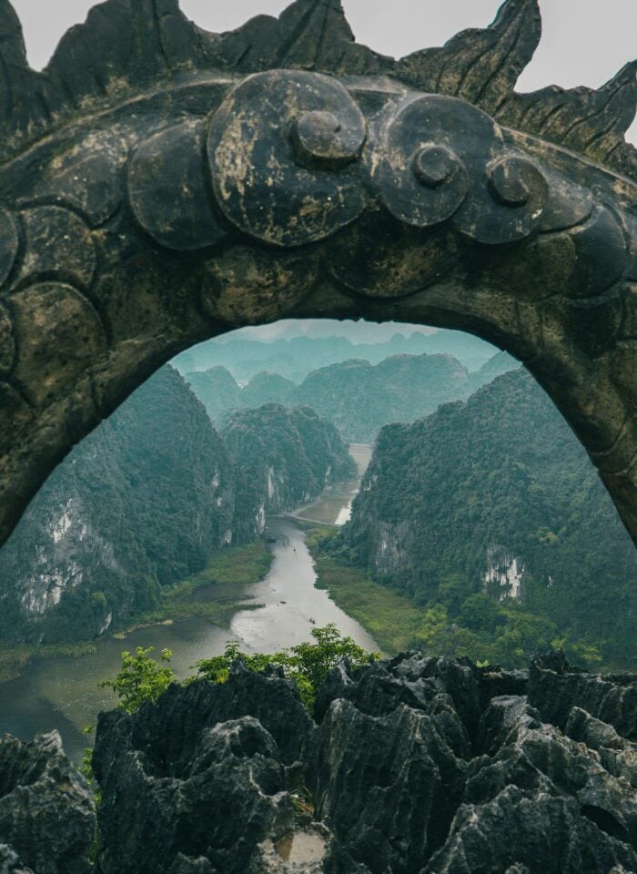 Limestone karst landscape and winding river framed by stone arch viewpoint in Ninh Bình Province, Vietnam.