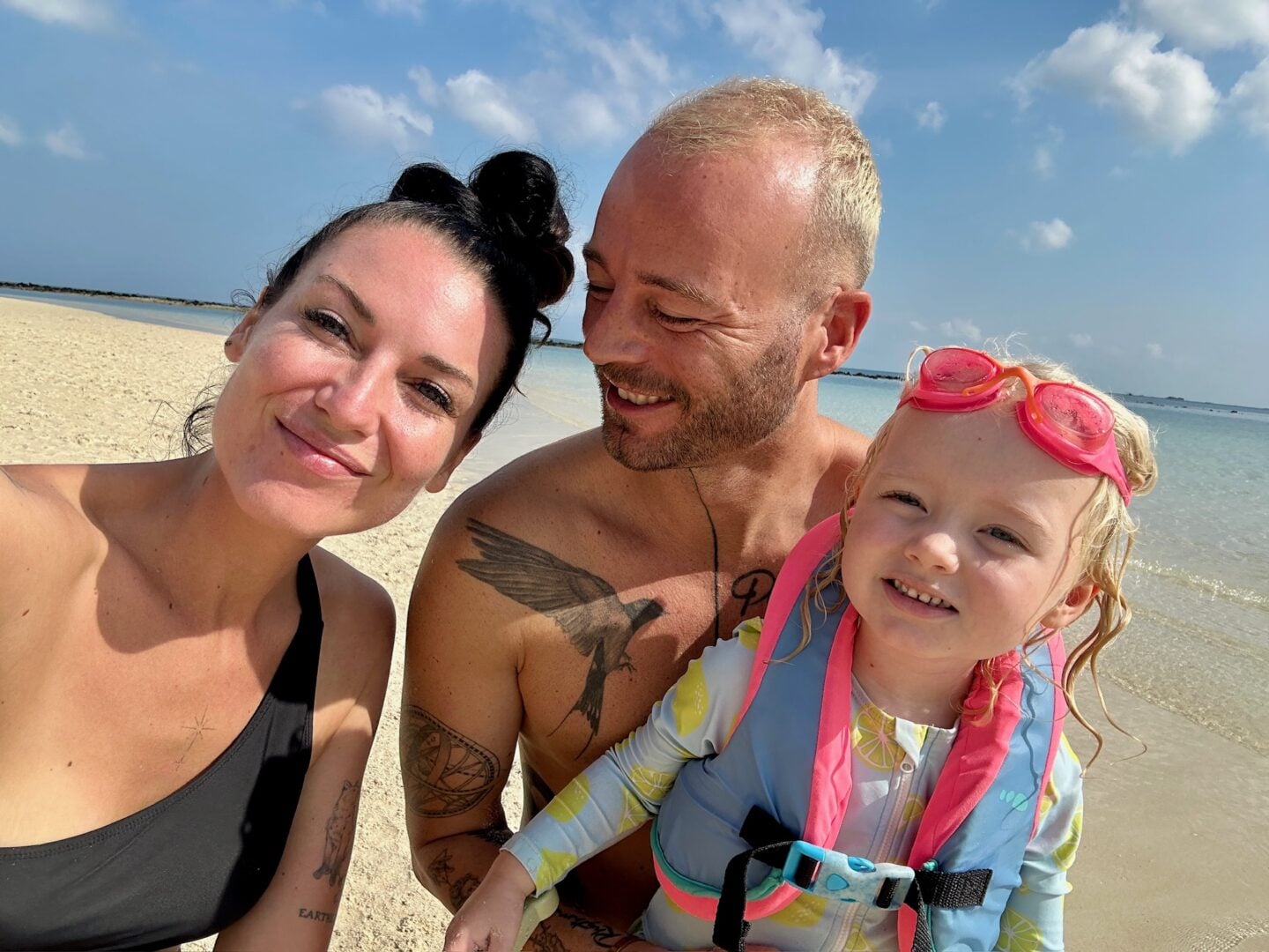 Family selfie at a shallow tropical beach in Thailand, with clear water, sandy shore, and bright daylight.