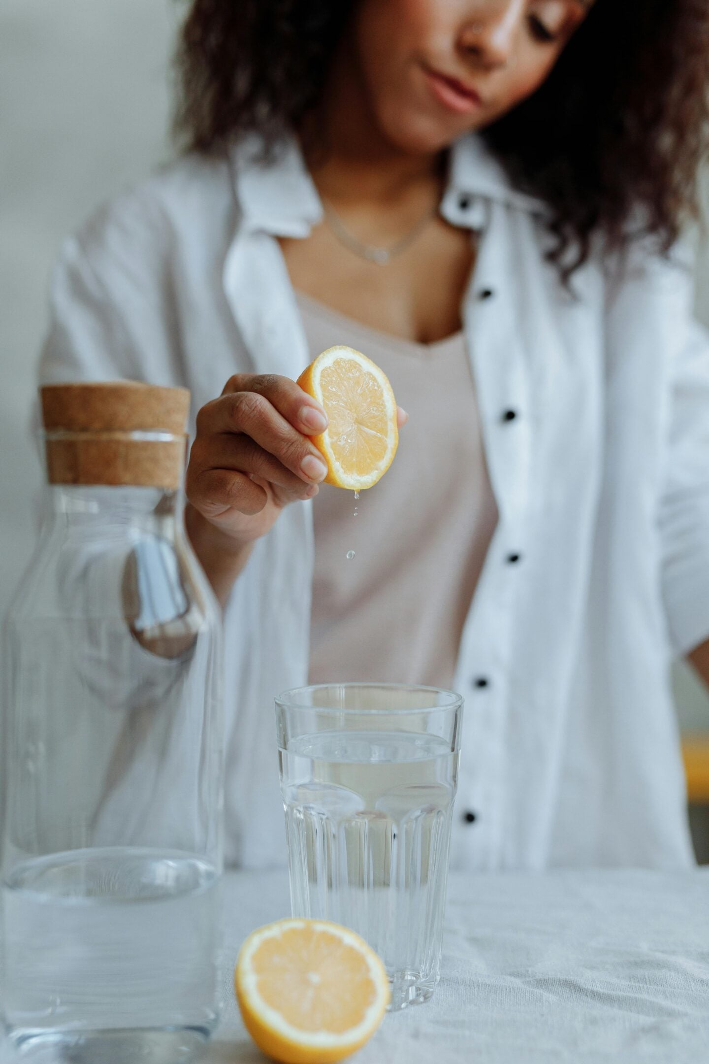 A woman squeezing fresh lemon juice into a glass of water, with a water carafe and lemon half on the table.