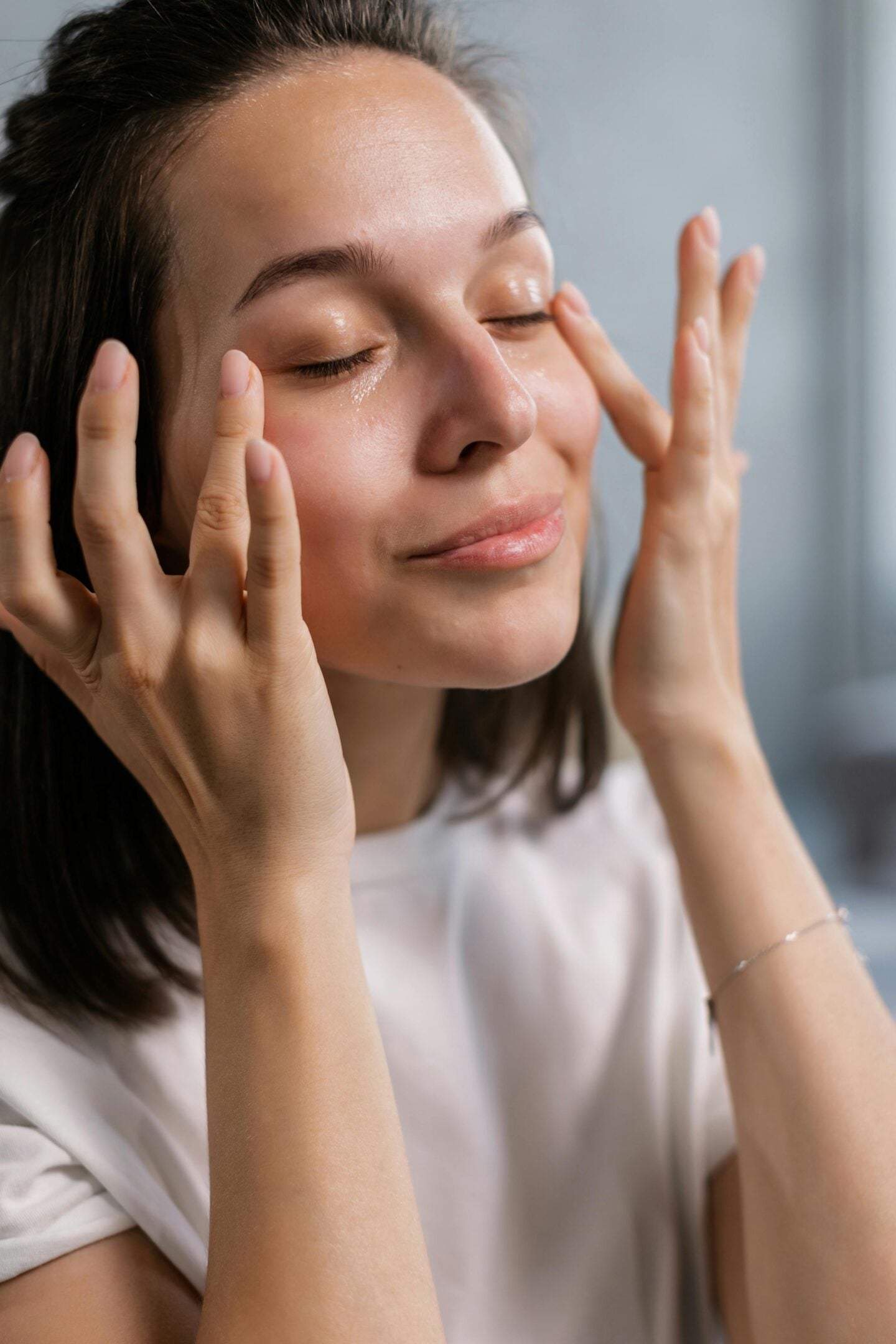 A woman gently massaging moisturizer into the skin around her eyes with a relaxed expression.
