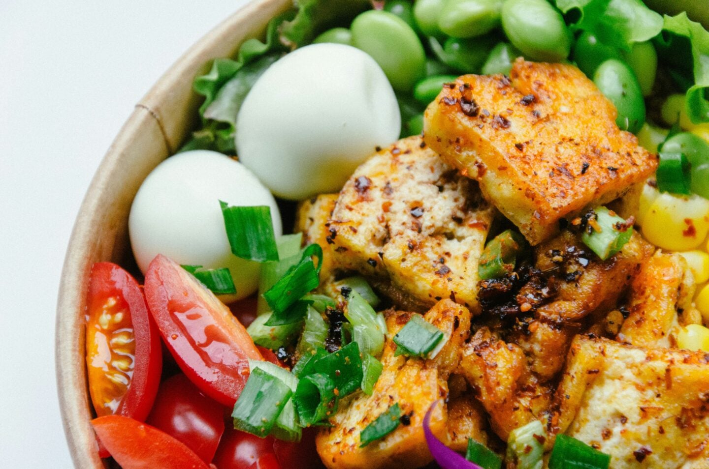 A colorful bowl of fresh ingredients including cherry tomatoes, boiled eggs, tofu, edamame, corn, and green onions.