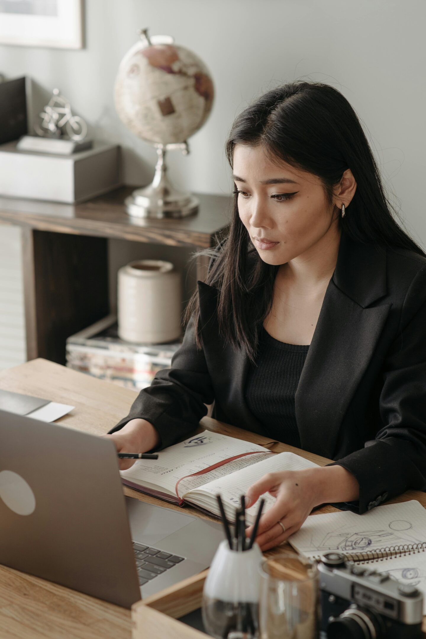 Businesswoman working on a laptop at a desk with a notebook and camera, planning finances for a travel-related business