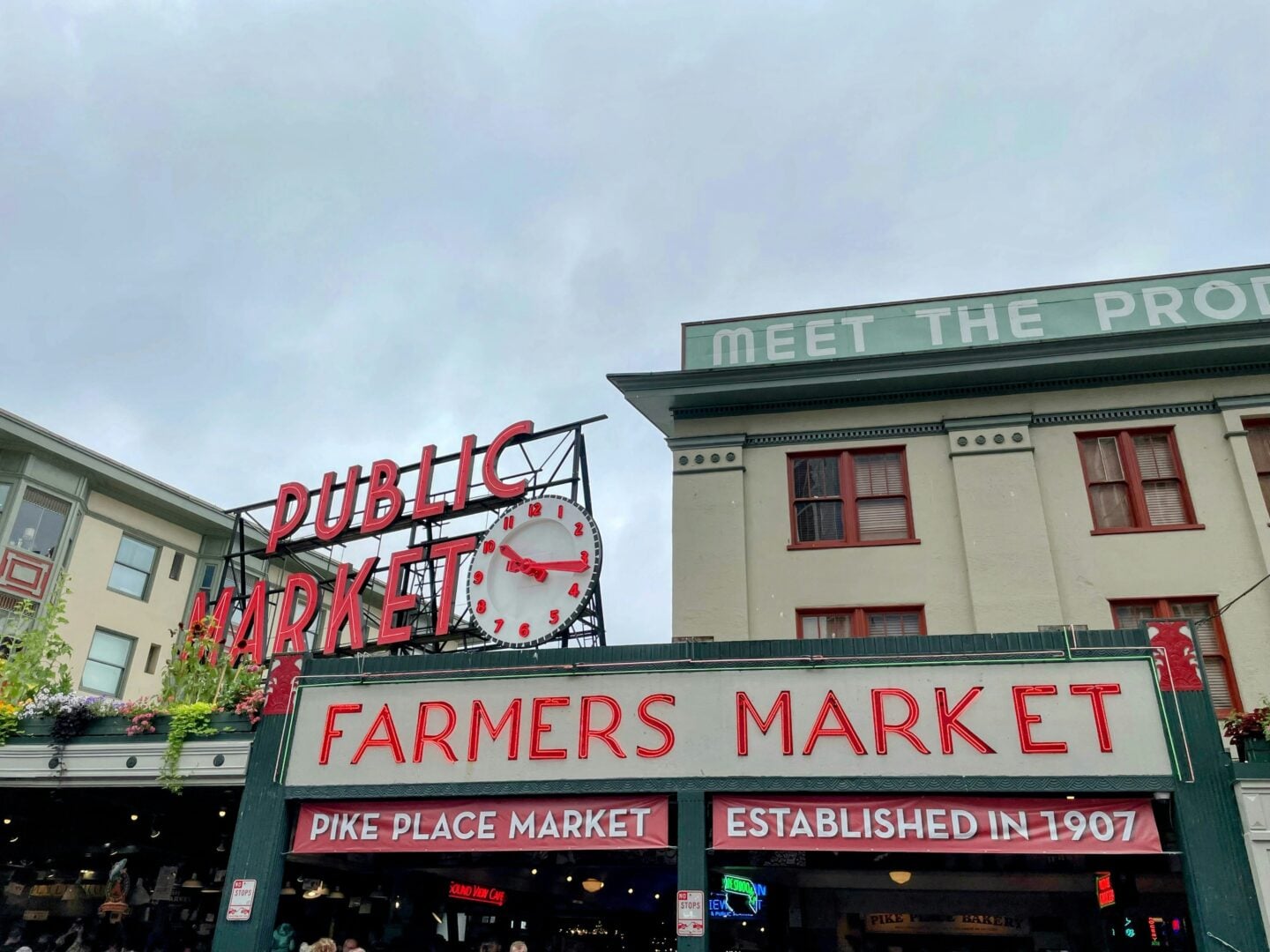 The iconic neon signs of Pike Place Market in Seattle, including the red “Public Market” clock and “Farmers Market” entrance.
