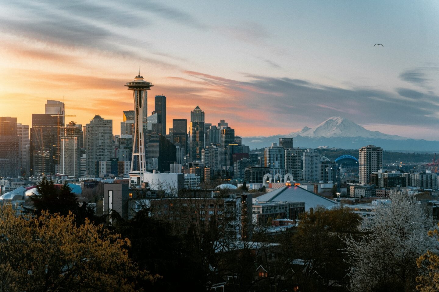 The Seattle skyline glows at sunset with the Space Needle in the foreground and Mount Rainier towering over the horizon.