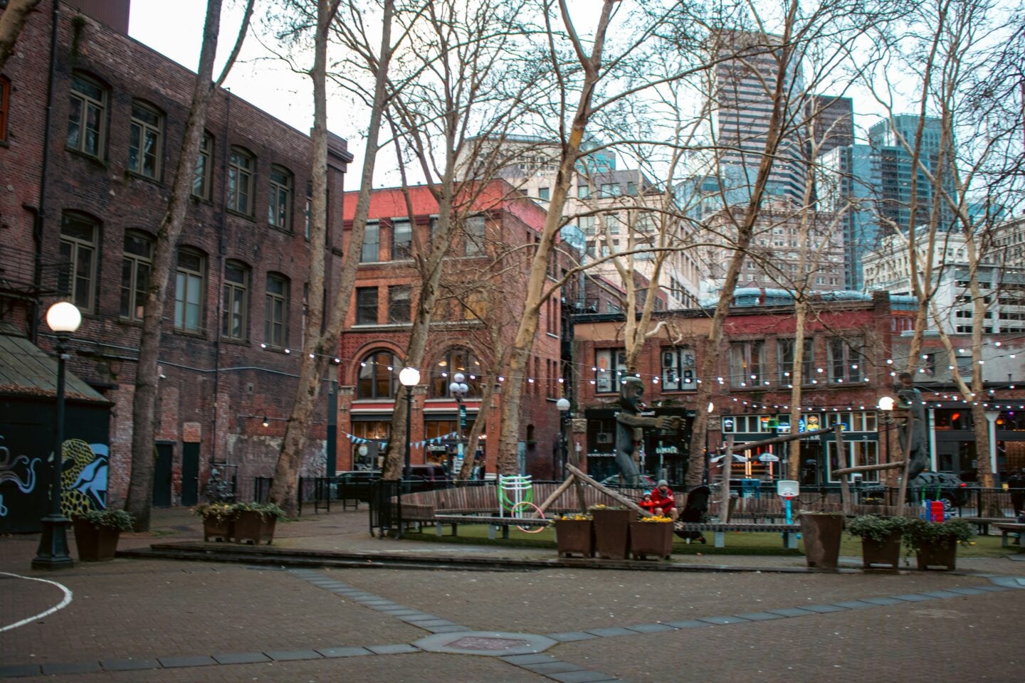 Historic brick buildings, leafless trees, and string lights decorating an open plaza in Seattle’s Pioneer Square district.