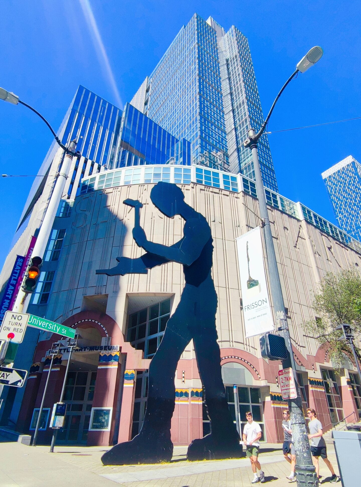 The Hammering Man sculpture stands in front of the Seattle Art Museum on a sunny day, with glass high-rise buildings towering behind it.