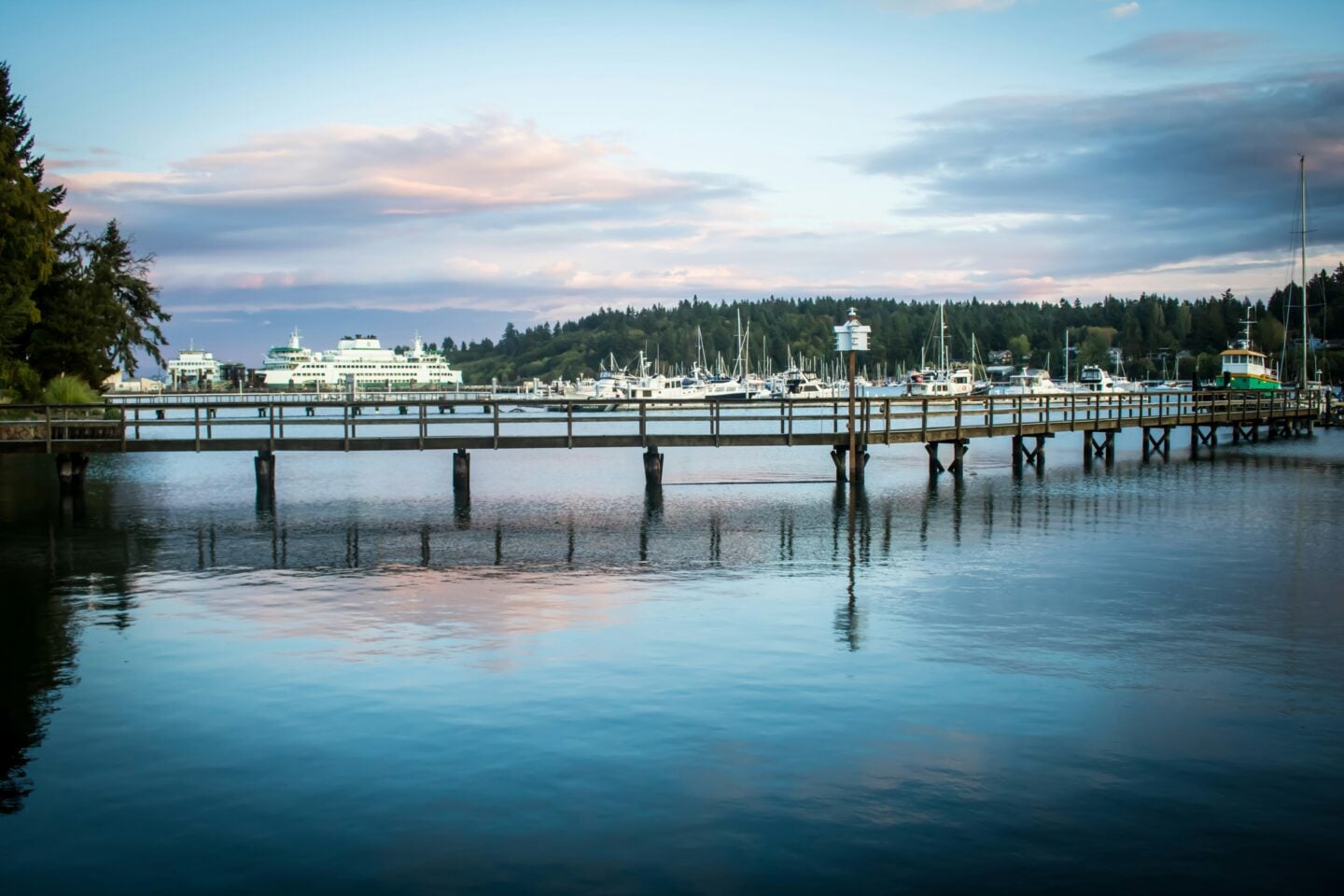 A peaceful waterfront scene with a wooden pier, moored boats, and a Washington State Ferry in the distance near Bainbridge Island.