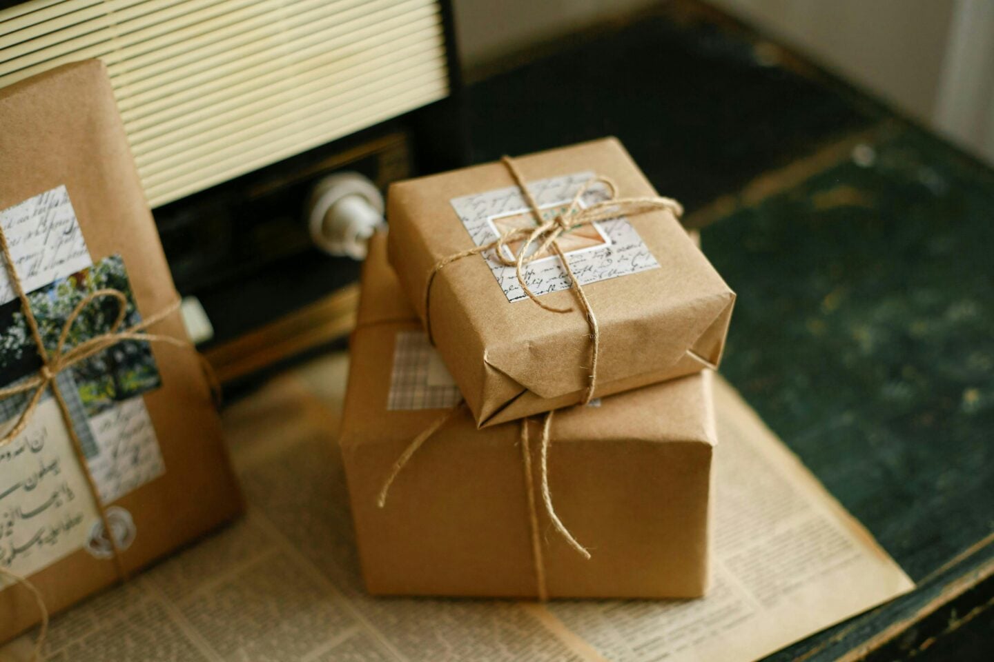 Beautifully wrapped gifts in brown kraft paper tied with twine, decorated with vintage-style labels, displayed on an old table with a retro radio in the background.