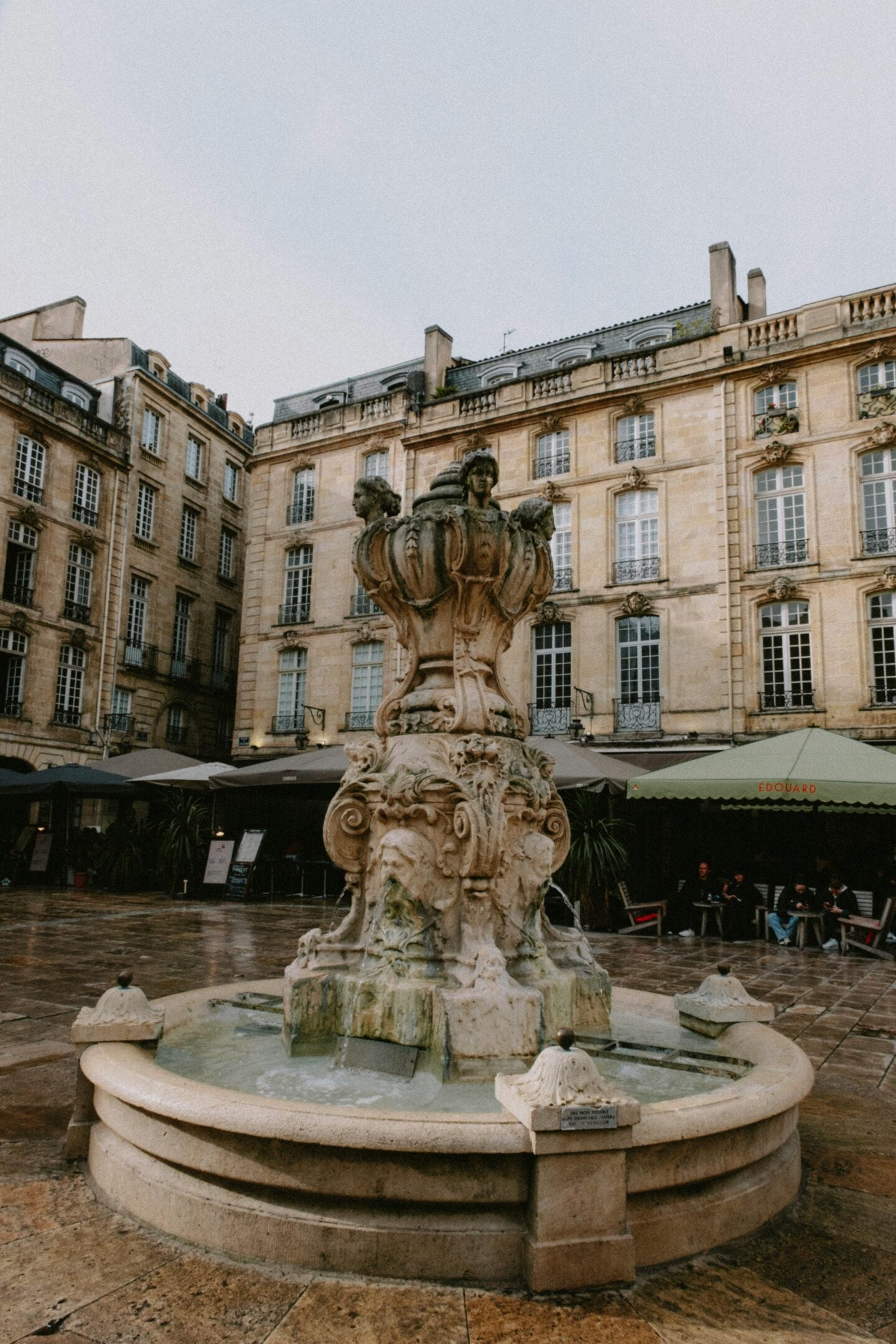 An ornate stone fountain at Place du Parlement in Bordeaux, surrounded by classic French architecture and outdoor cafés.