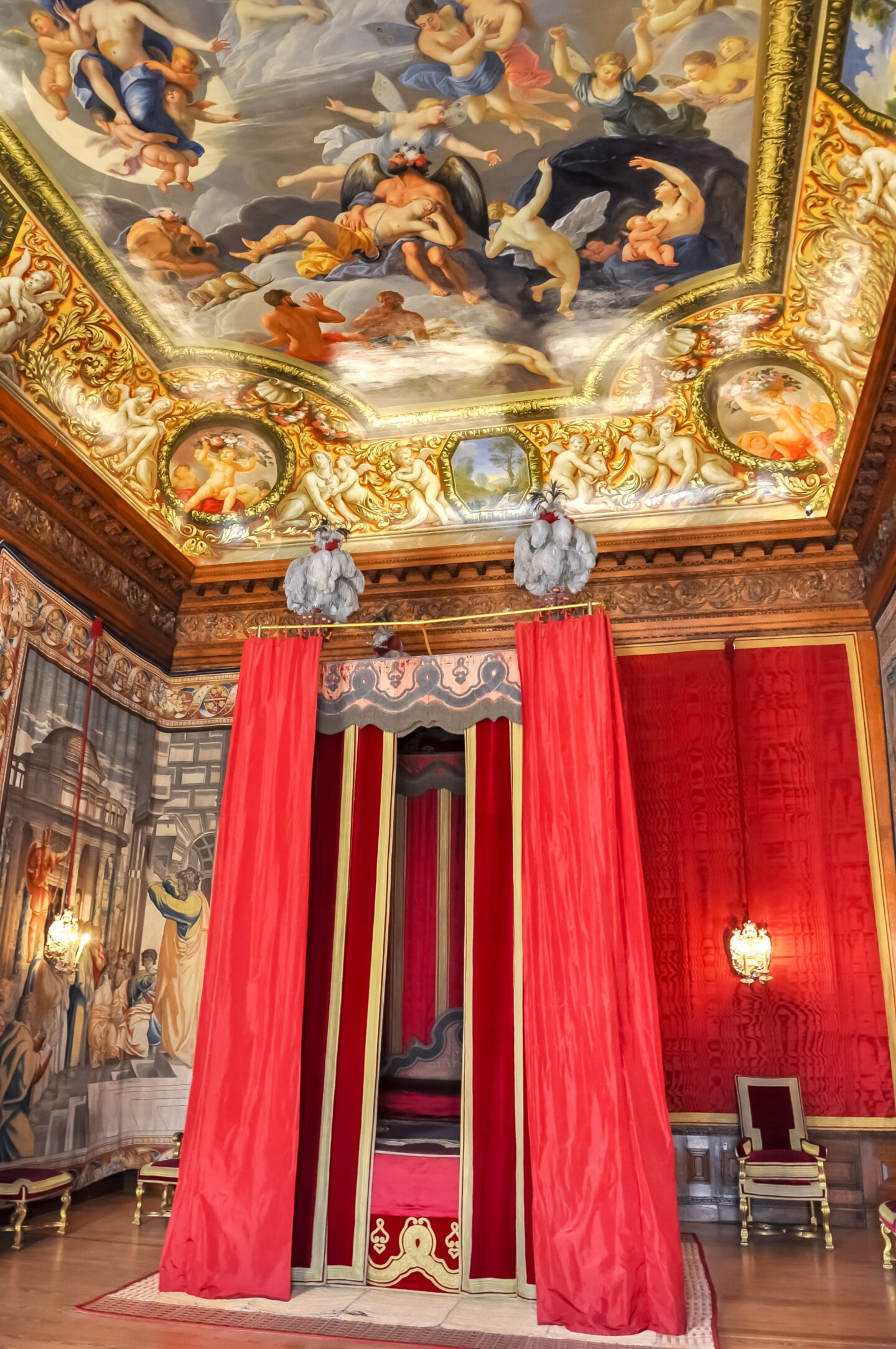 William III’s state bedchamber and painted ceiling - lavish royal bedchamber at Hampton Court Palace with red velvet bed curtains, gilded wall decorations, and an ornate painted ceiling filled with mythological scenes and cherubs.