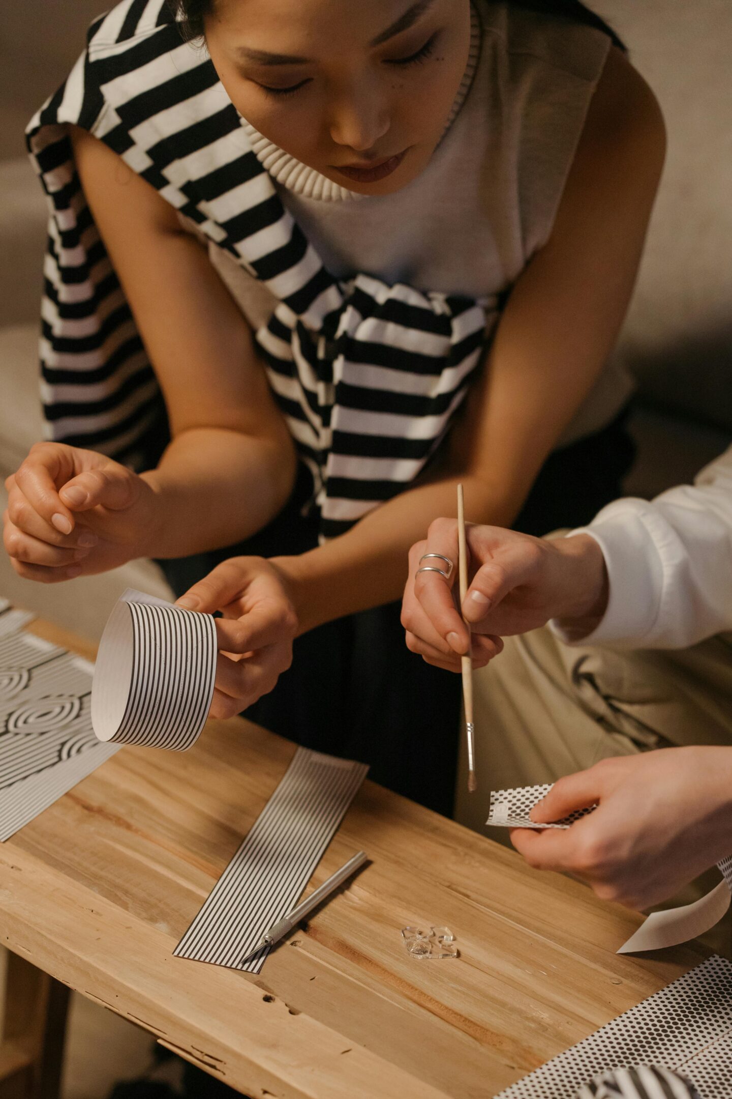 People working together on a DIY craft project using paper strips and tools on a wooden table, promoting sustainable living