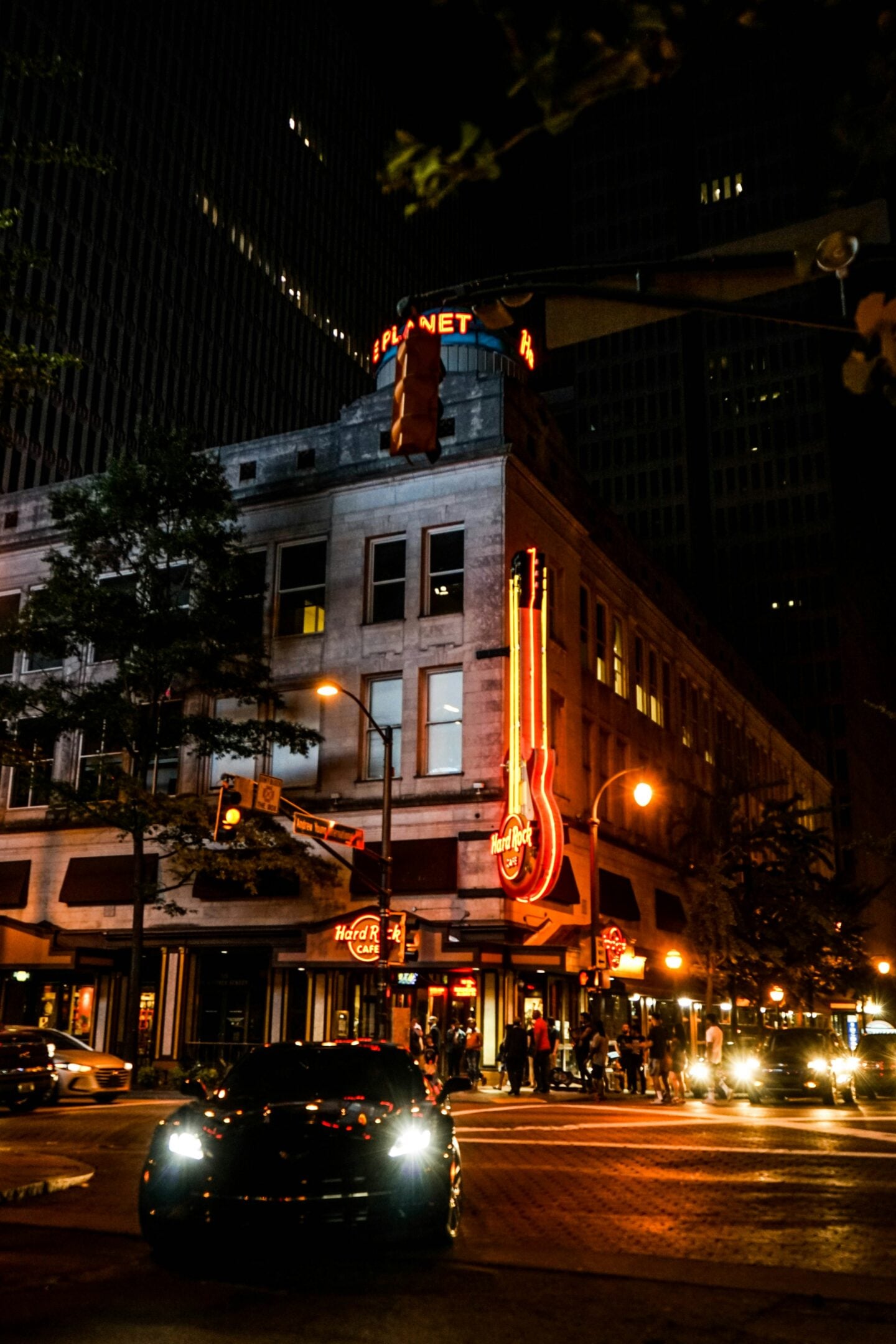 A nighttime street scene outside the Hard Rock Café in downtown Atlanta, with neon lights and passing cars.