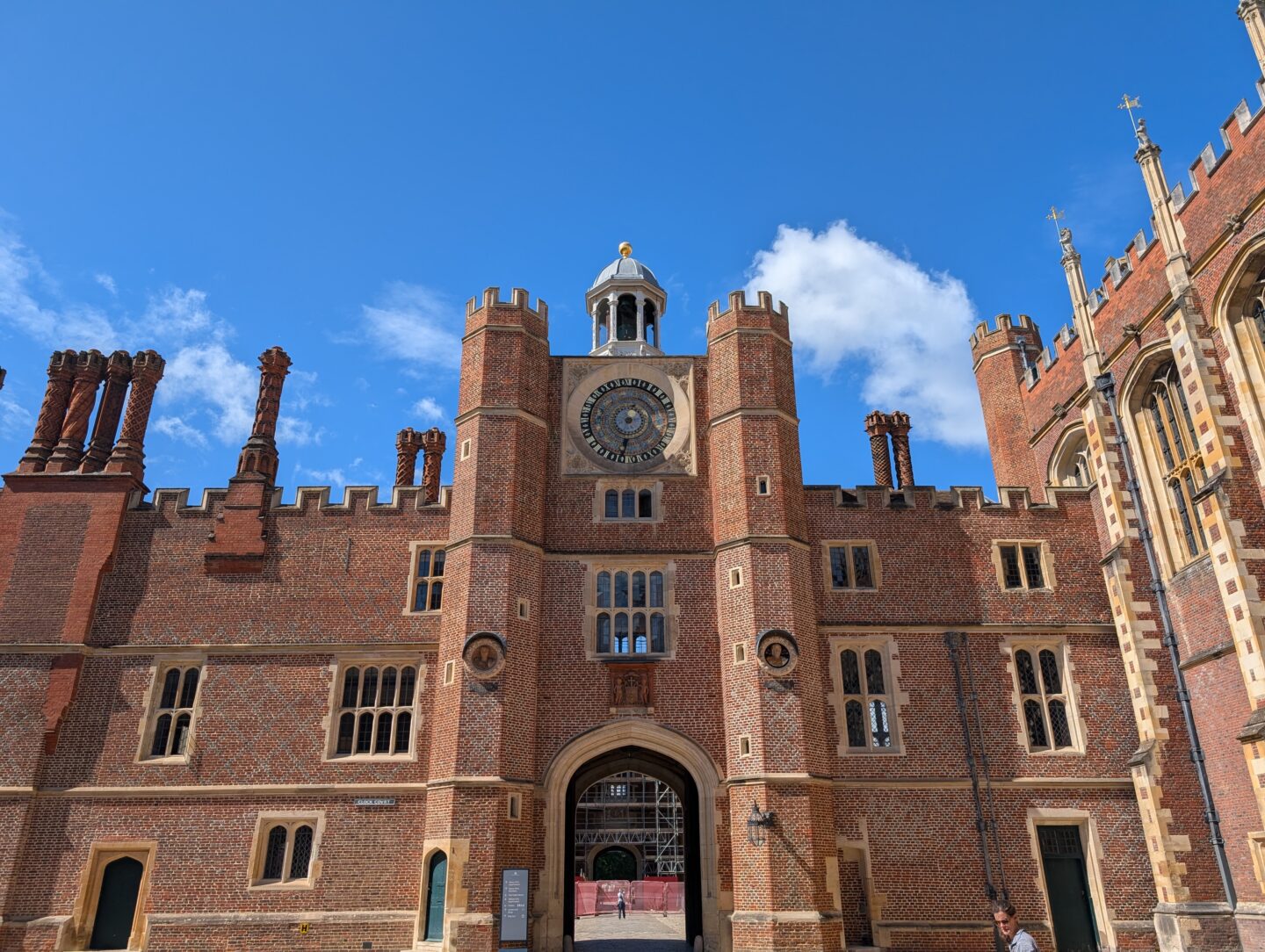 The Tudor Astronomical Clock on the gatehouse at Hampton Court Palace, surrounded by decorative brickwork, chimneys, and battlements on a sunny day.