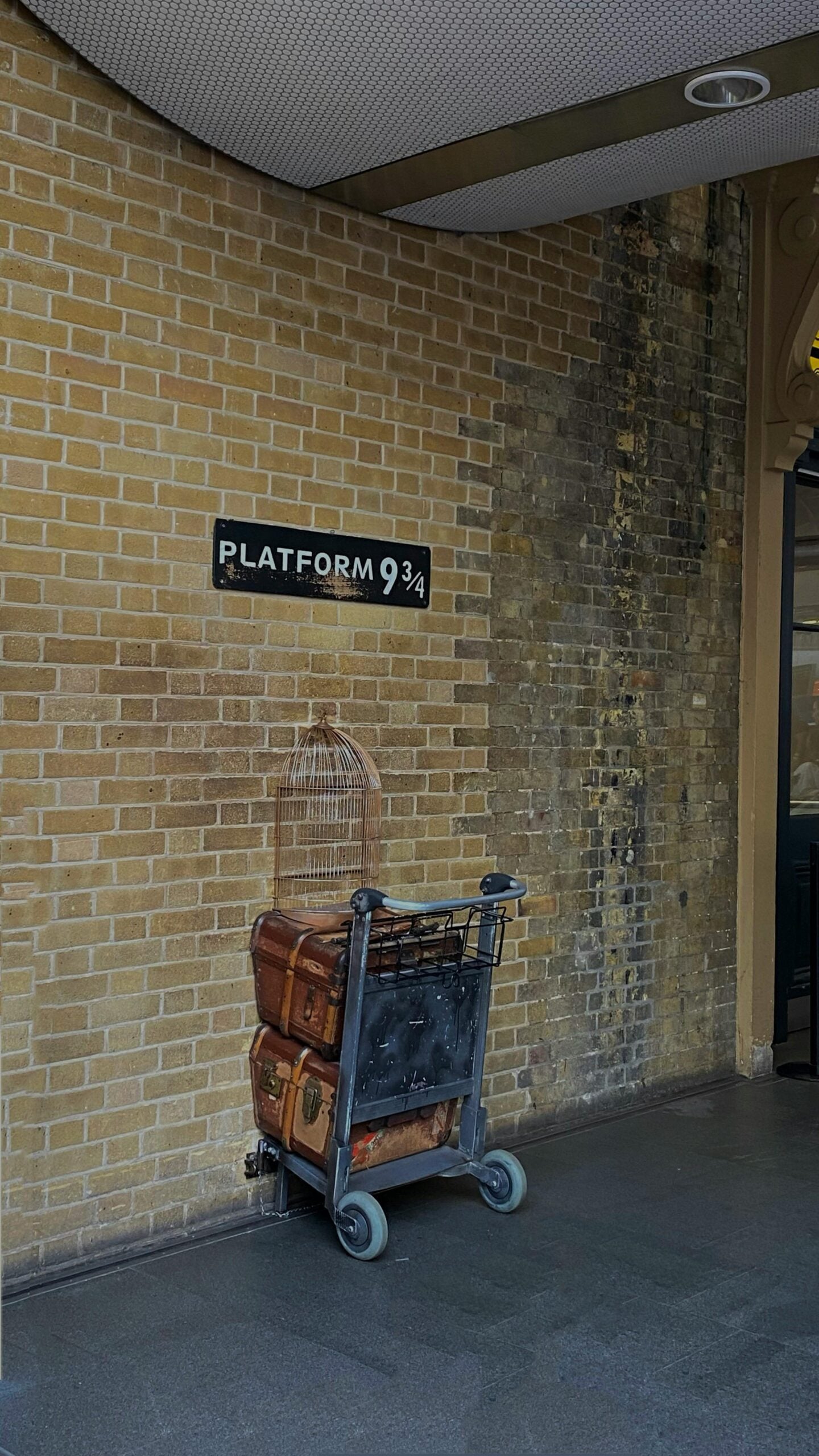 Platform 9¾ photo spot at King’s Cross Station in London with a luggage trolley and birdcage.