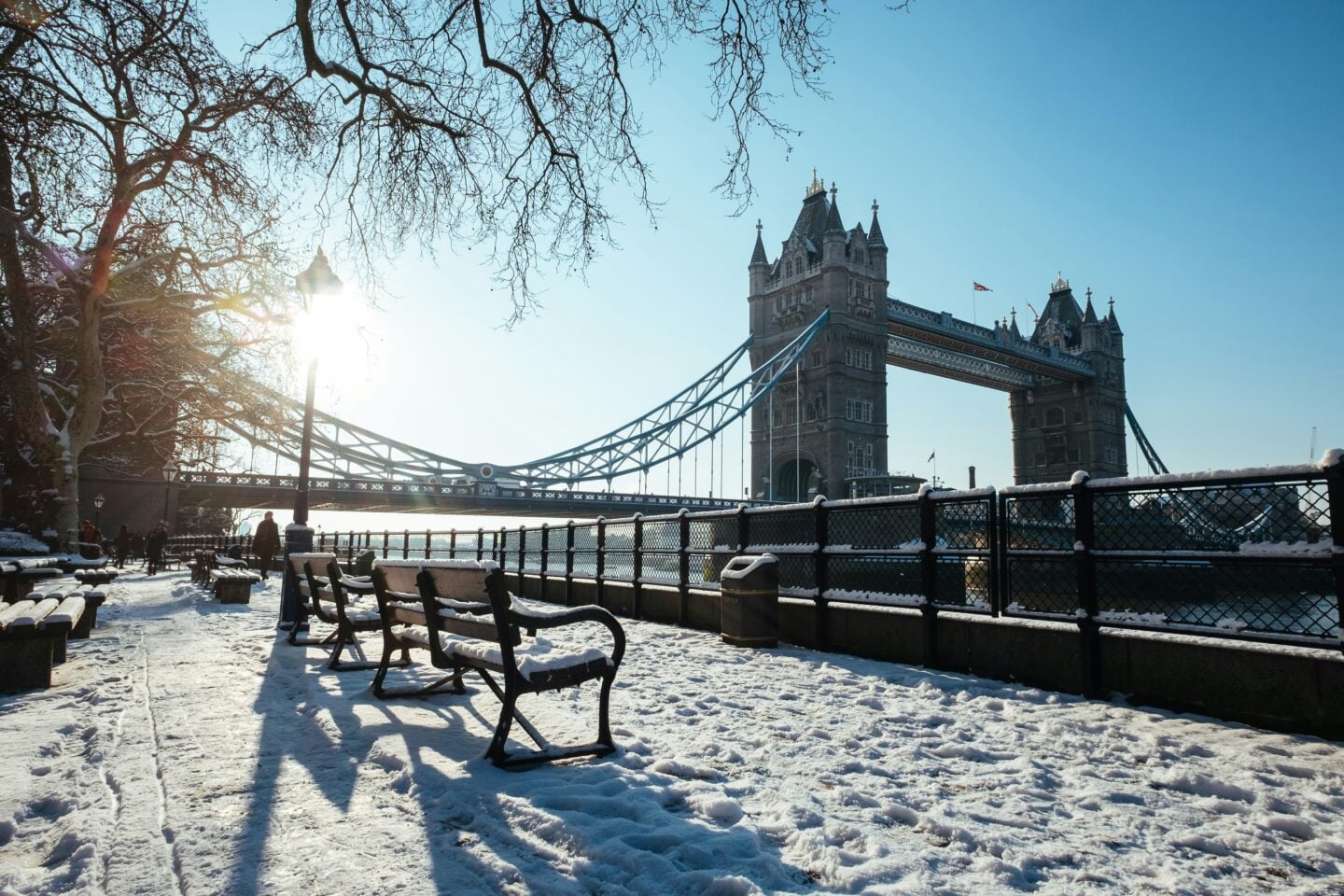Snow-covered walkway along the River Thames with Tower Bridge in the background on a bright winter morning.