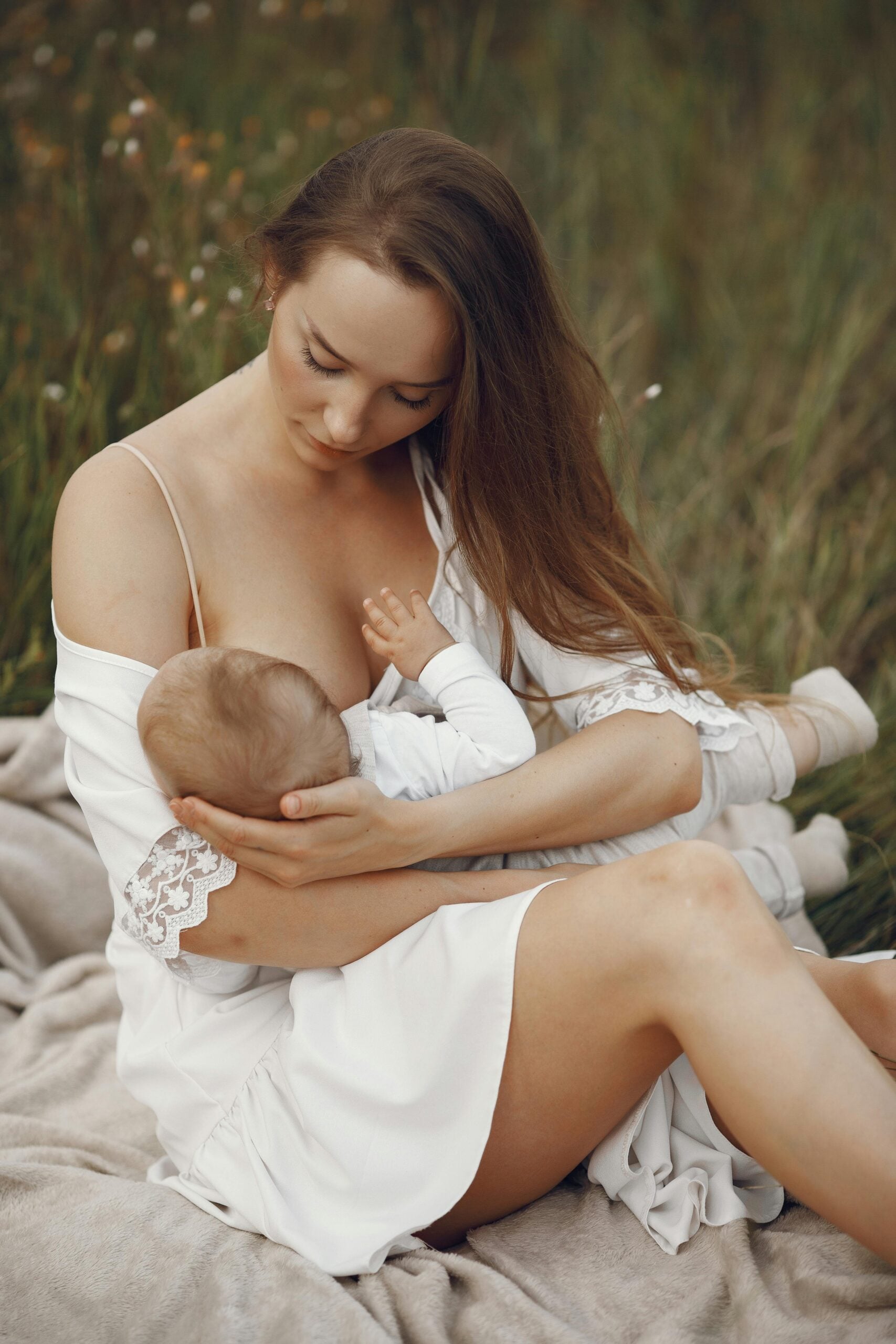 Mother breastfeeding her baby outdoors on a blanket in a meadow