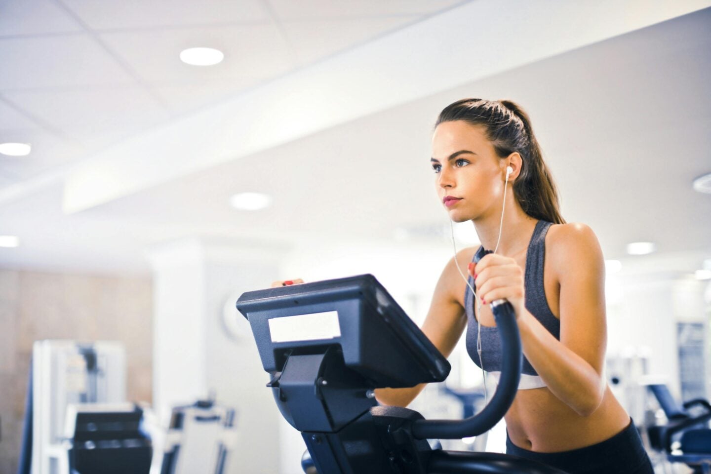 A woman exercising on a cardio machine at the gym while listening to music through earphones.