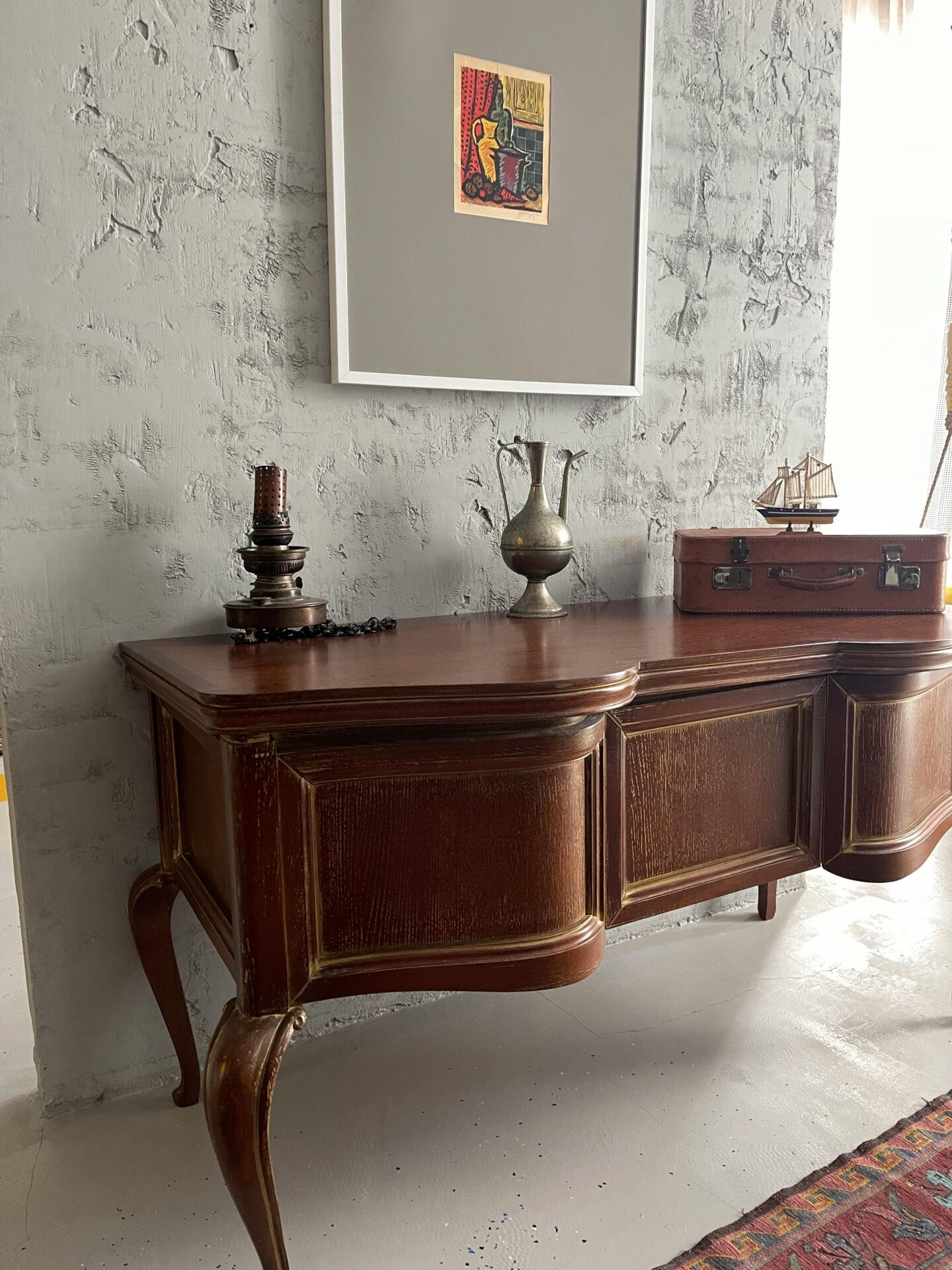 Vintage wooden sideboard with curved legs and paneled doors, styled with antique decor against a textured gray wall.
