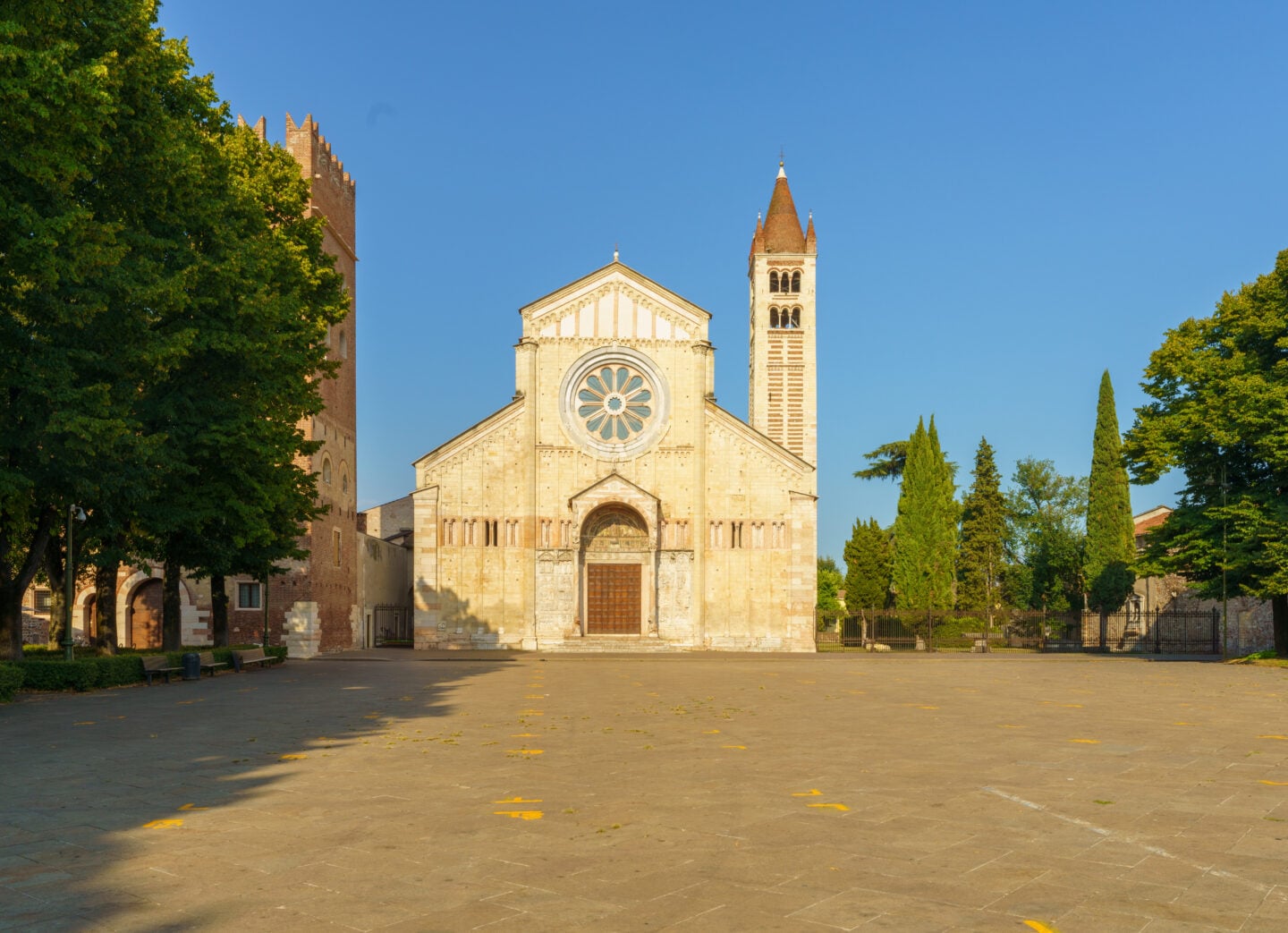Front view of the Basilica of San Zeno Maggiore in Verona, featuring Romanesque architecture, stone façade, and bell tower under a clear blue sky.