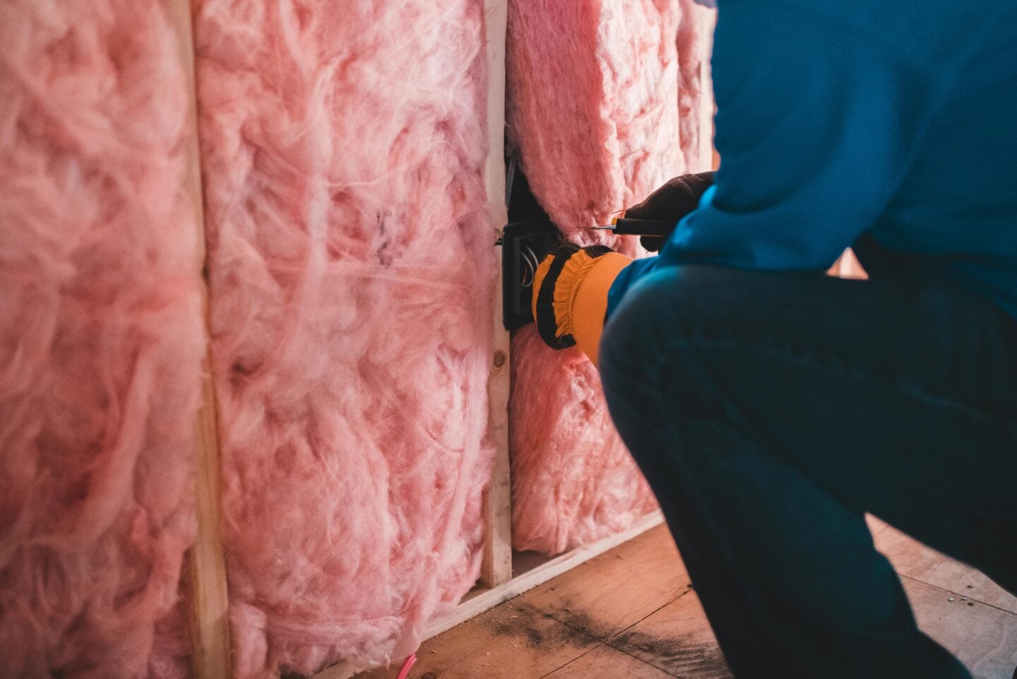 Worker installing pink fiberglass insulation inside a wall during home renovation
