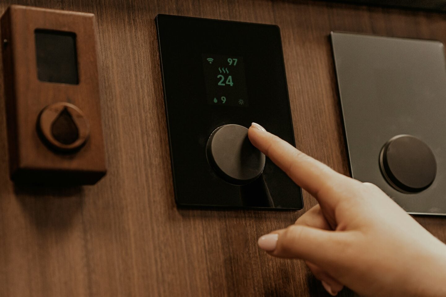 Hand adjusting a smart thermostat mounted on a wooden wall