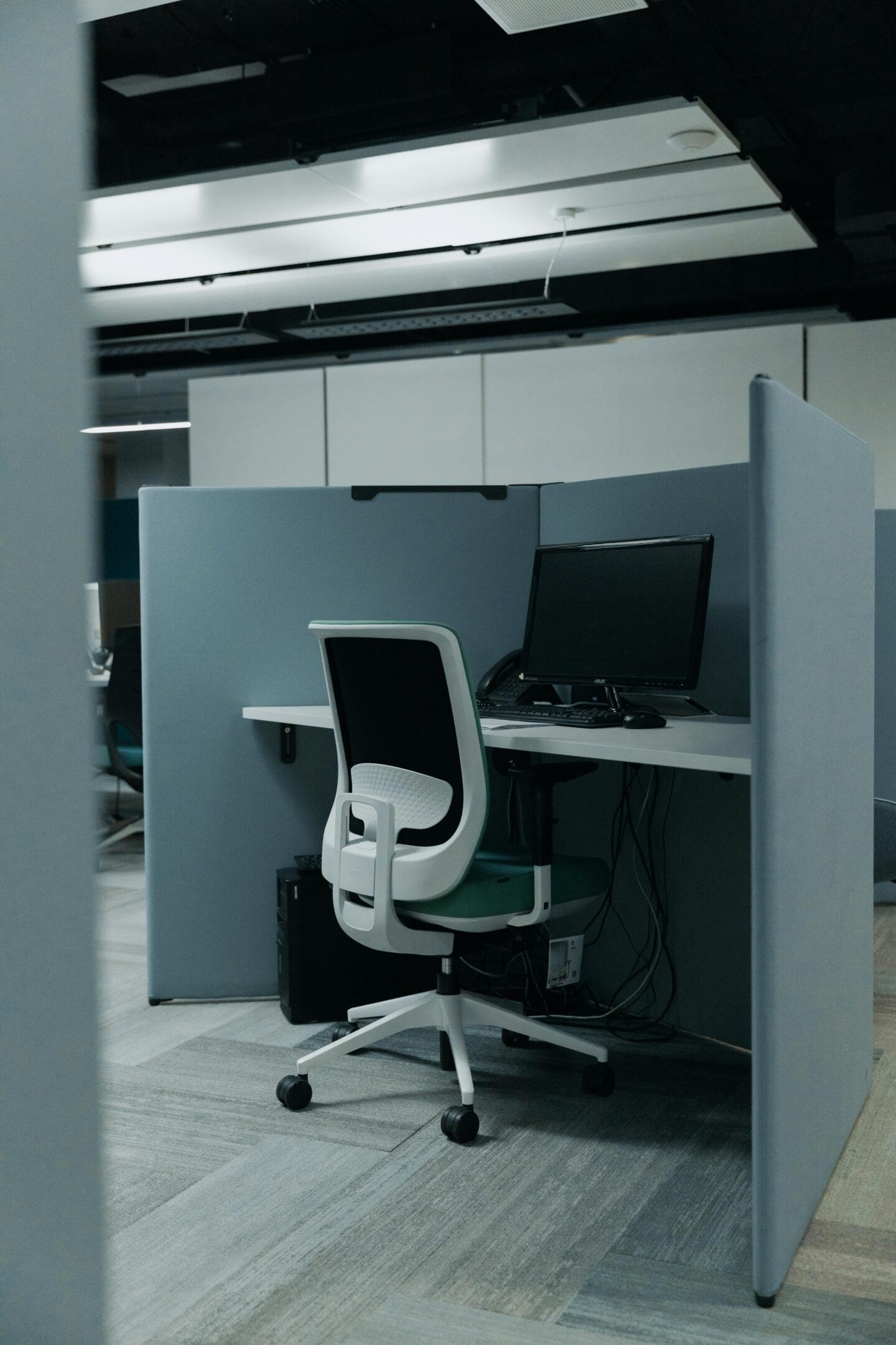 Modern office cubicle with desk, computer monitor and ergonomic chair, showing the use of partition panels as room dividers to create private work zones in a corporate workspace.