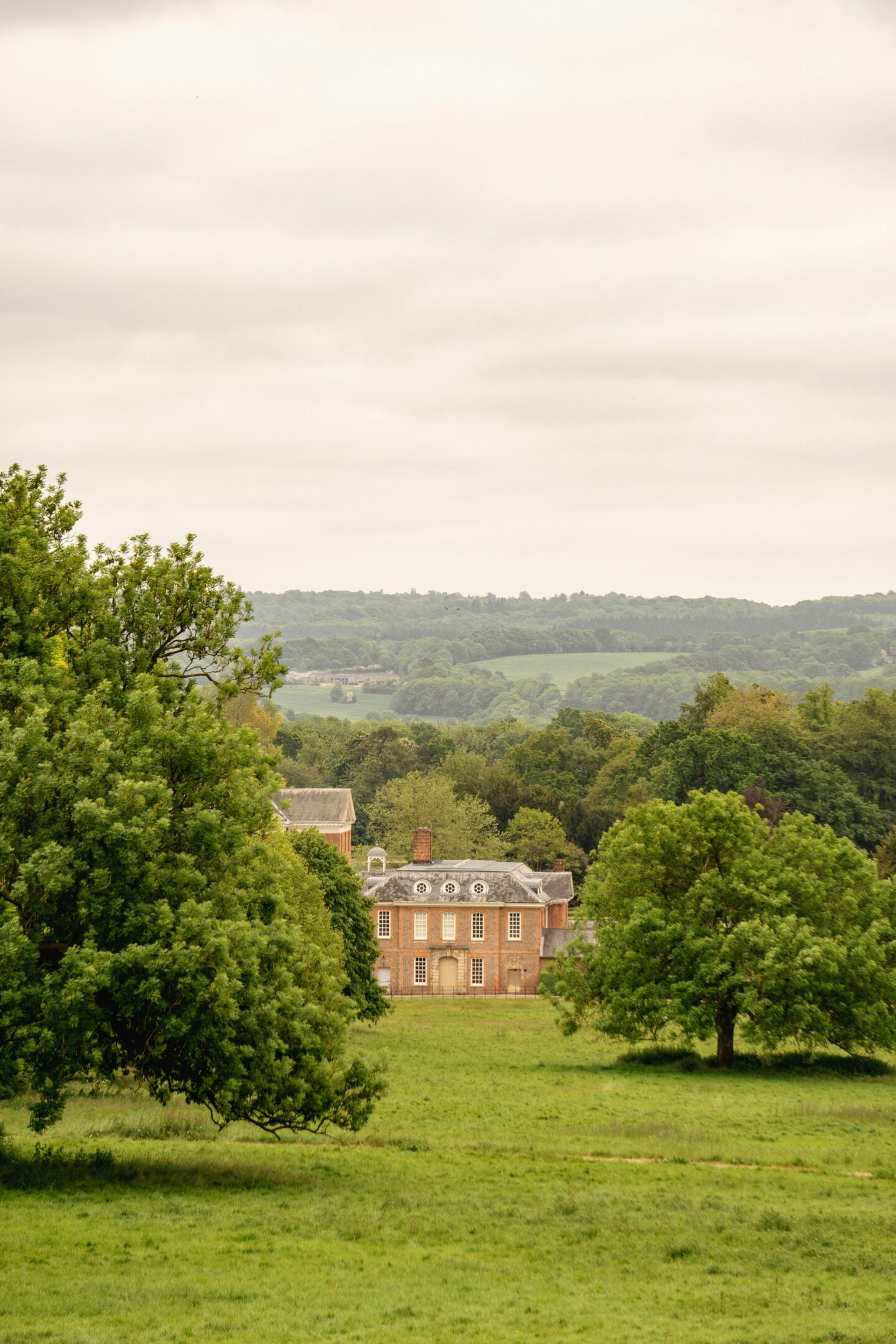 Historic country house nestled among trees and open fields, overlooking rolling hills and rural landscape.