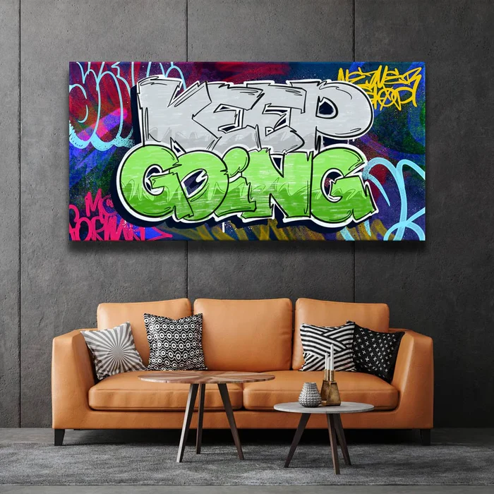 A modern living room with a tan leather sofa and patterned cushions, featuring a large, colorful graffiti-style wall art that reads “KEEP GOING” in bold white and green letters against a vibrant street-art background.