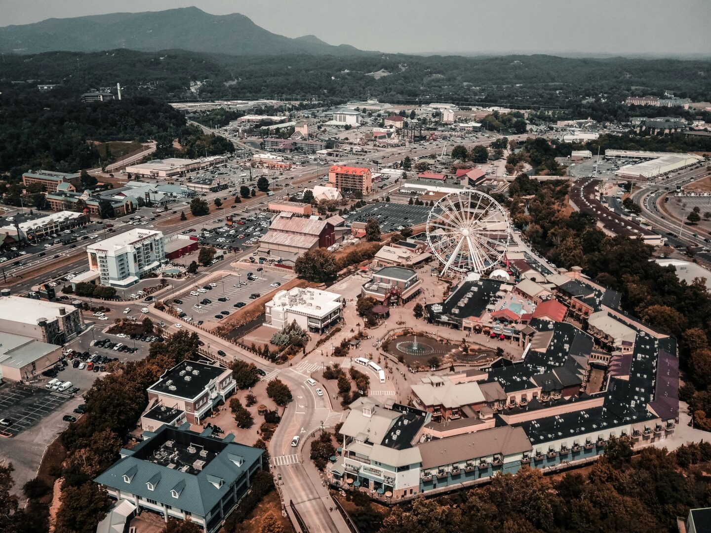 Aerial view of Pigeon Forge, Tennessee, featuring the Great Smoky Mountain Wheel, Parkway attractions, hotels and surrounding mountain landscape.