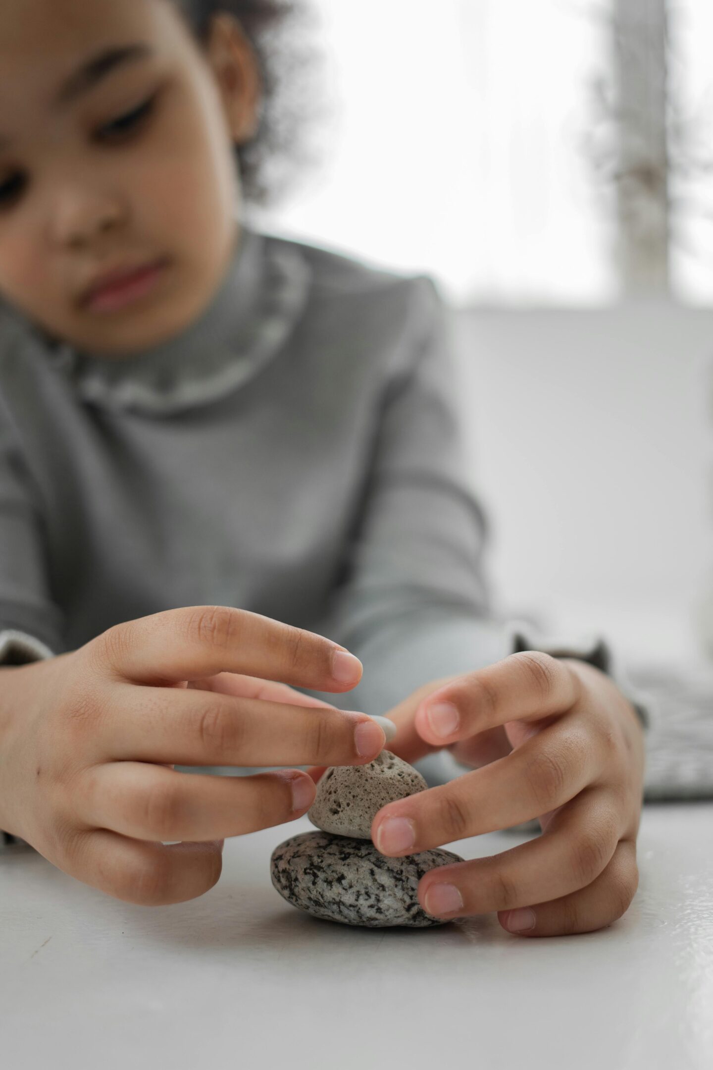 Close-up of a child’s hands gently balancing small stones on top of each other indoors.