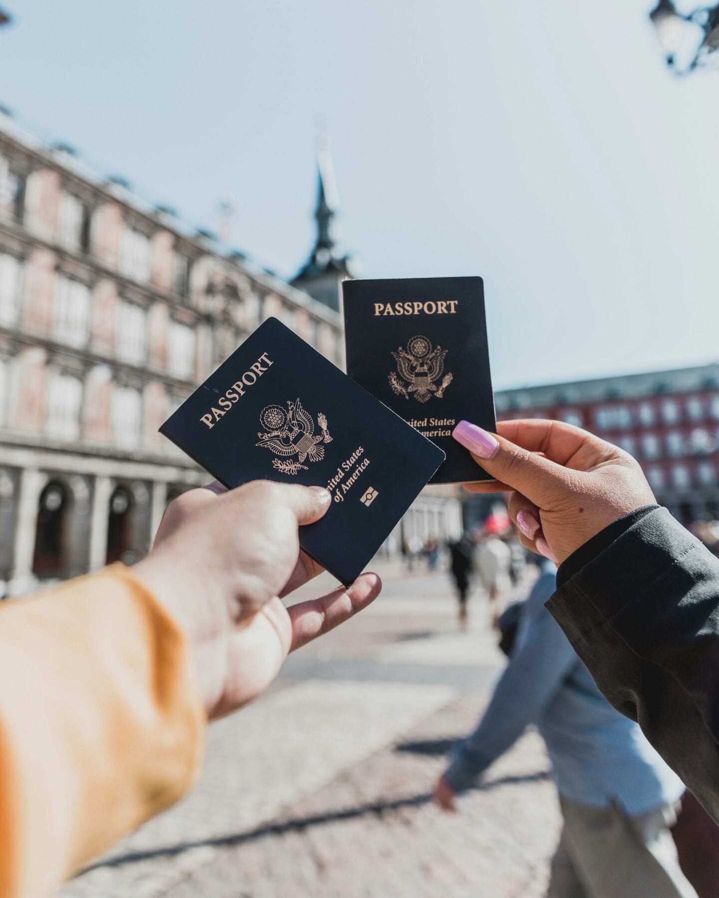 Two people holding U.S. passports outdoors in a city square, preparing for international travel.