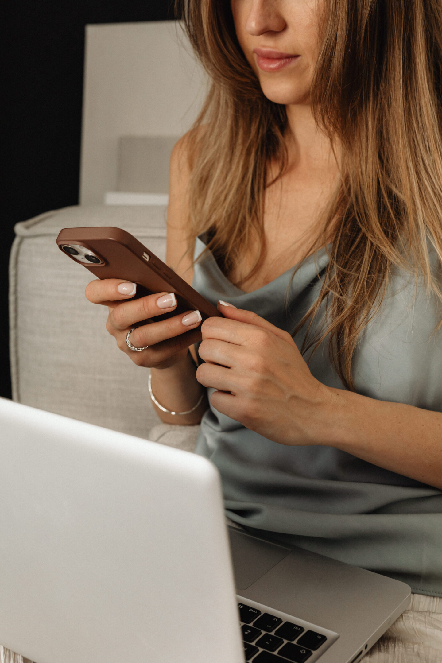 Woman checking her phone while working on a laptop in a modern home office
