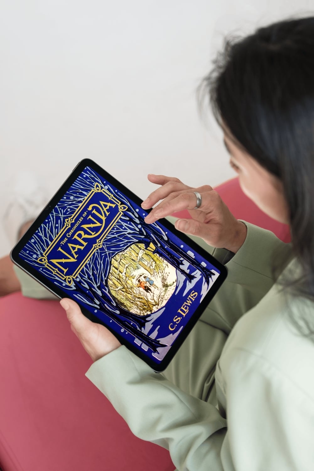 Person holding a tablet and reading an ebook of The Chronicles of Narnia by C. S. Lewis, shown on the screen with illustrated cover art.
