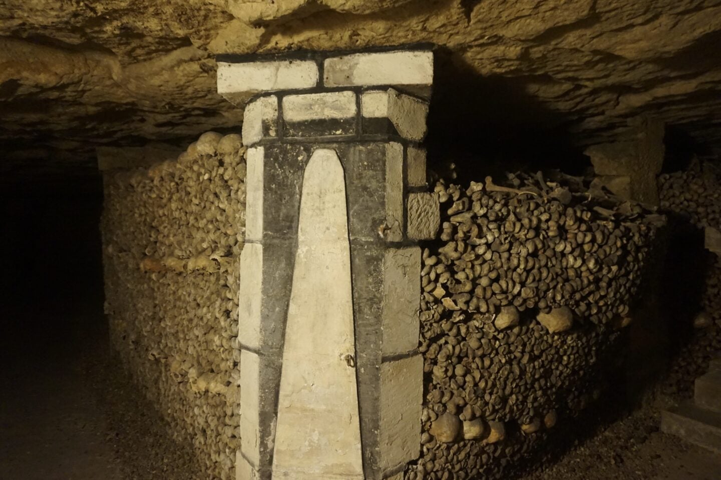 Stacked human bones and stone pillar inside the Paris Catacombs, one of the real-life locations that influenced the unsettling setting of As Above, So Below.