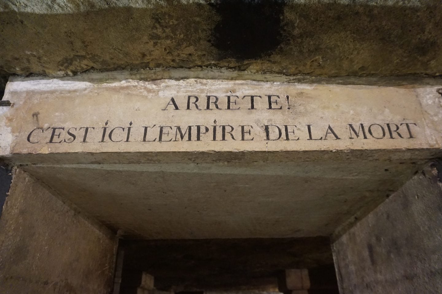 Stone inscription inside the Paris Catacombs reading “Arrête! C’est ici l’empire de la mort,” the real underground tunnels that inspired the horror film As Above, So Below.