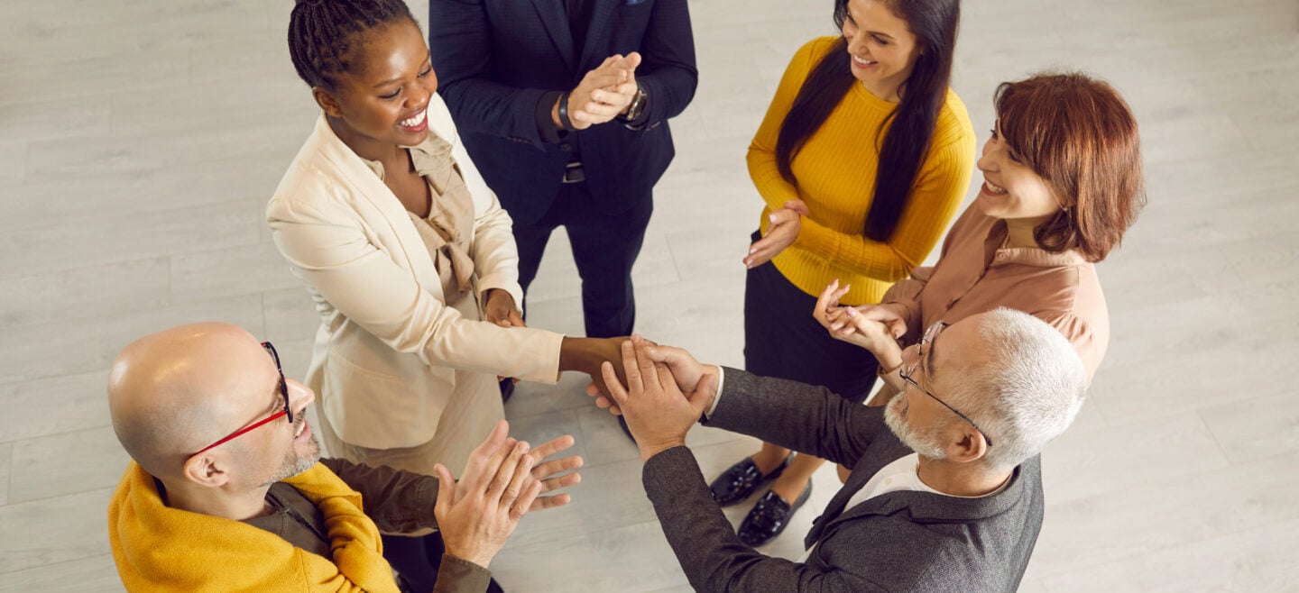 A diverse group of professionals standing in a circle, smiling and applauding during a casual business networking meeting