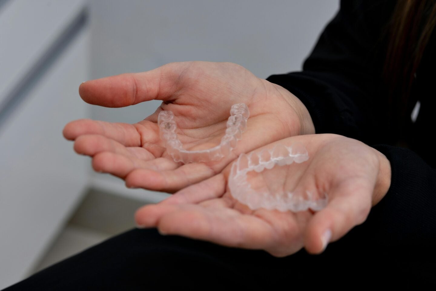 A person holding two clear mouth night guards in their open hands.
