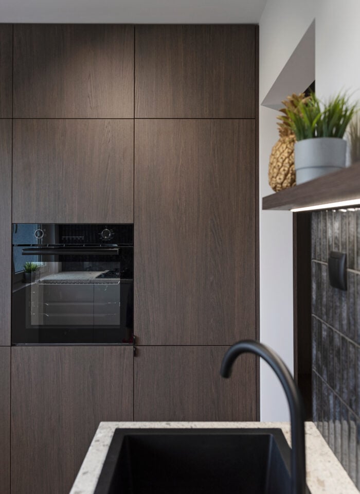 Modern kitchen with kitchen sink and dark tiles on the wall and wooden furniture with oven.