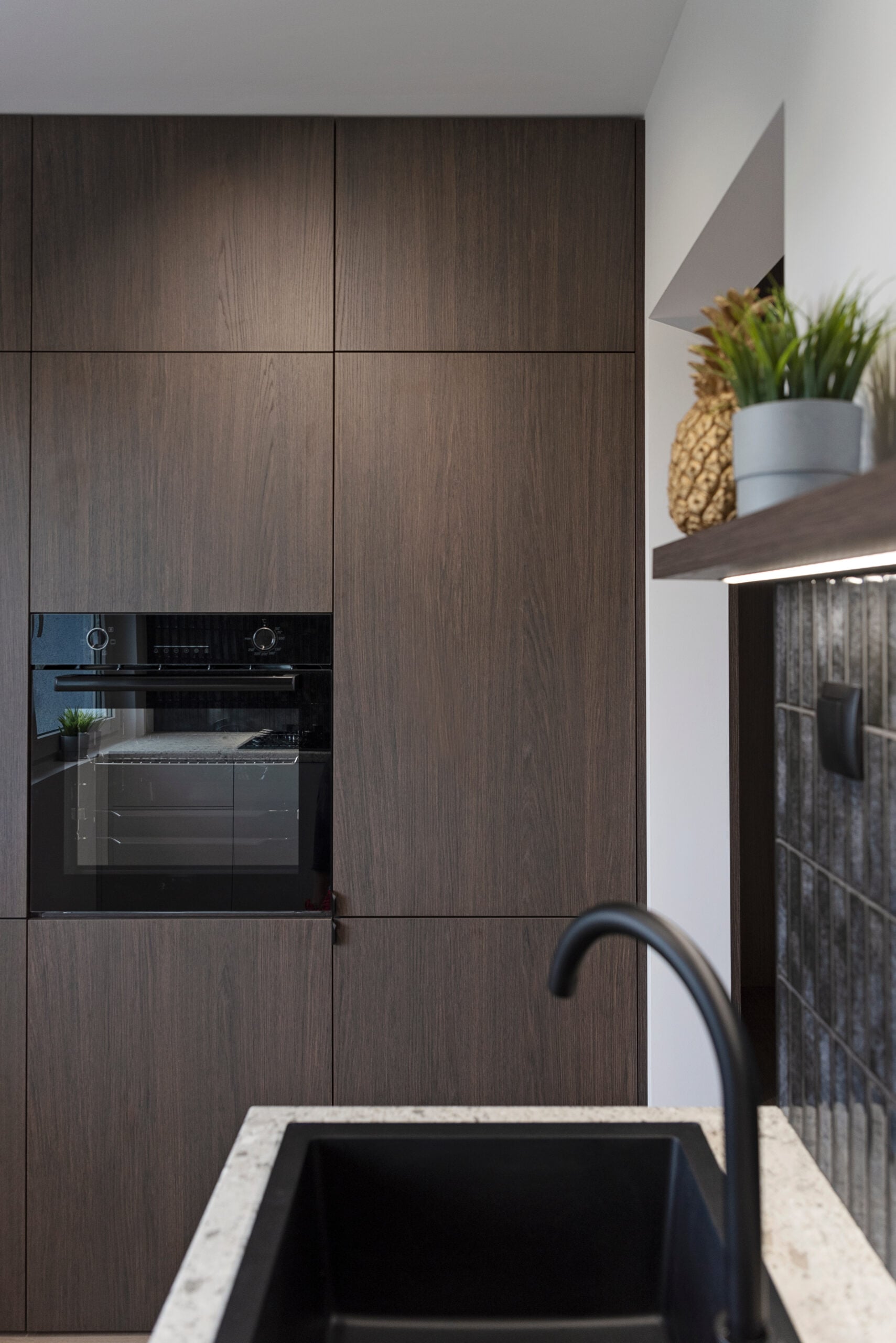 Modern kitchen with kitchen sink and dark tiles on the wall and wooden furniture with oven.