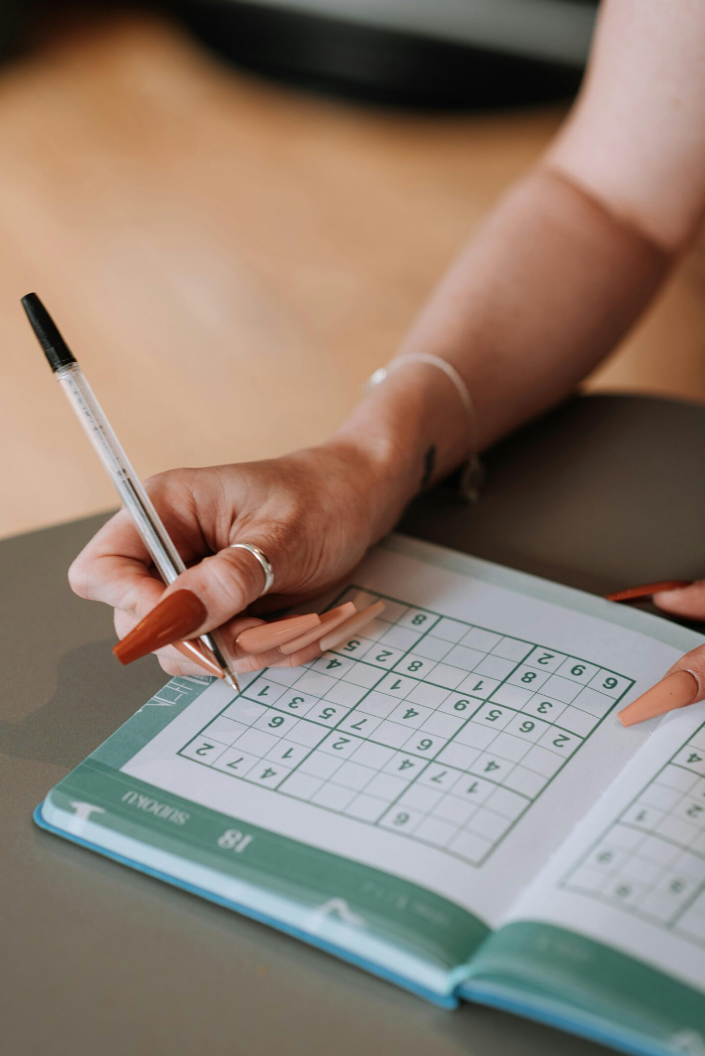 Person solving a number puzzle in a puzzle book with a pen
