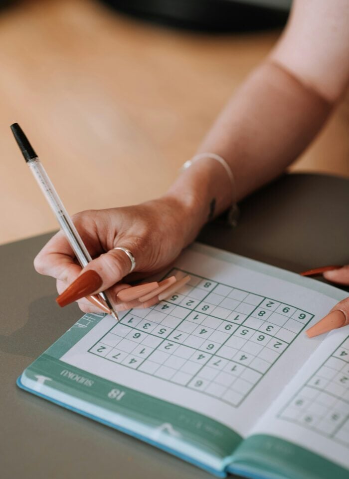 Person solving a number puzzle in a puzzle book with a pen