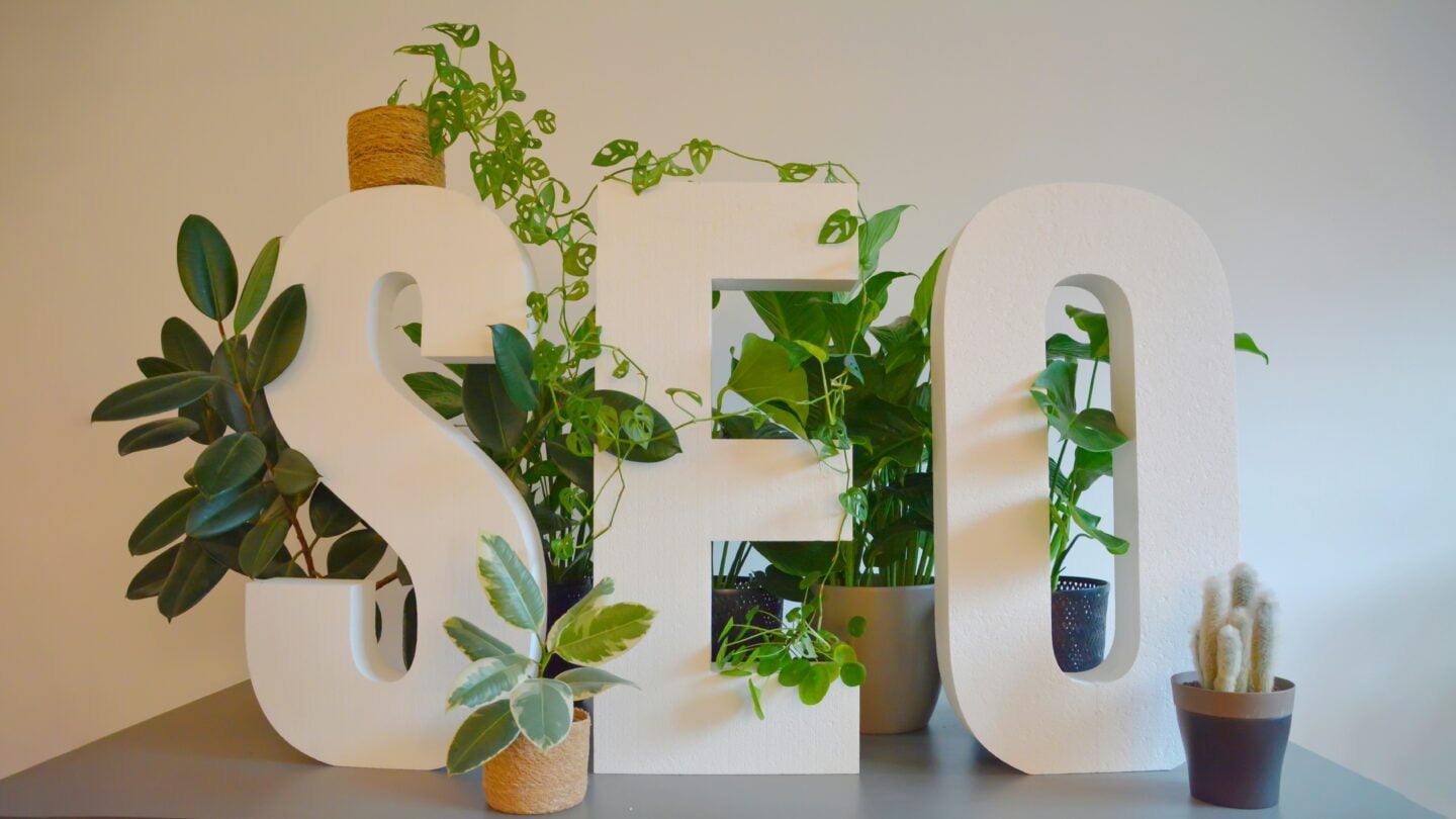 Large white letters spelling SEO decorated with green indoor plants on a modern office desk.
